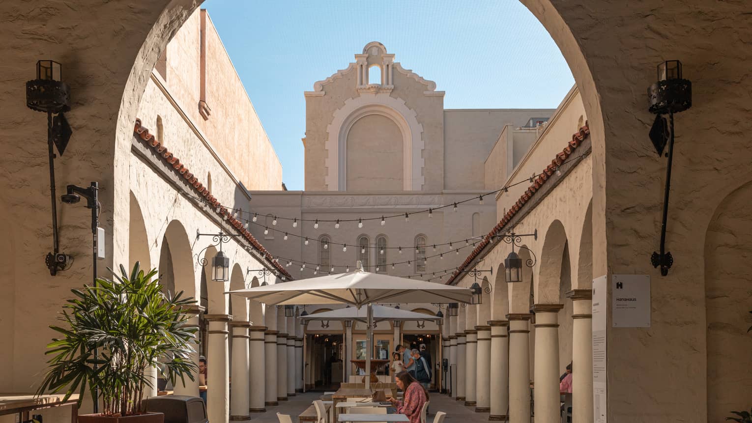 An archway leading to a small street with columns and surrounded by small tan buildings.