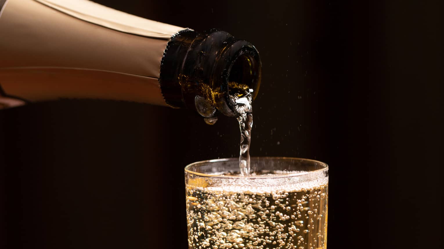 A bottle of champagne is poured into a glass as bubbles float to the top