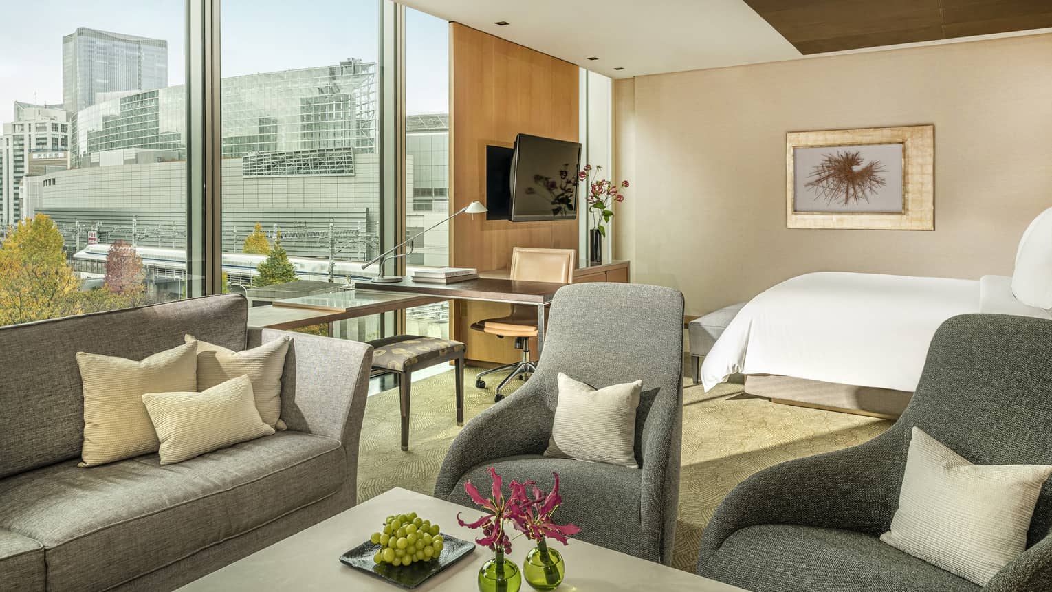 Junior suite with gray sofa, armchairs, work desk by a window with plaza view and king bed in the background