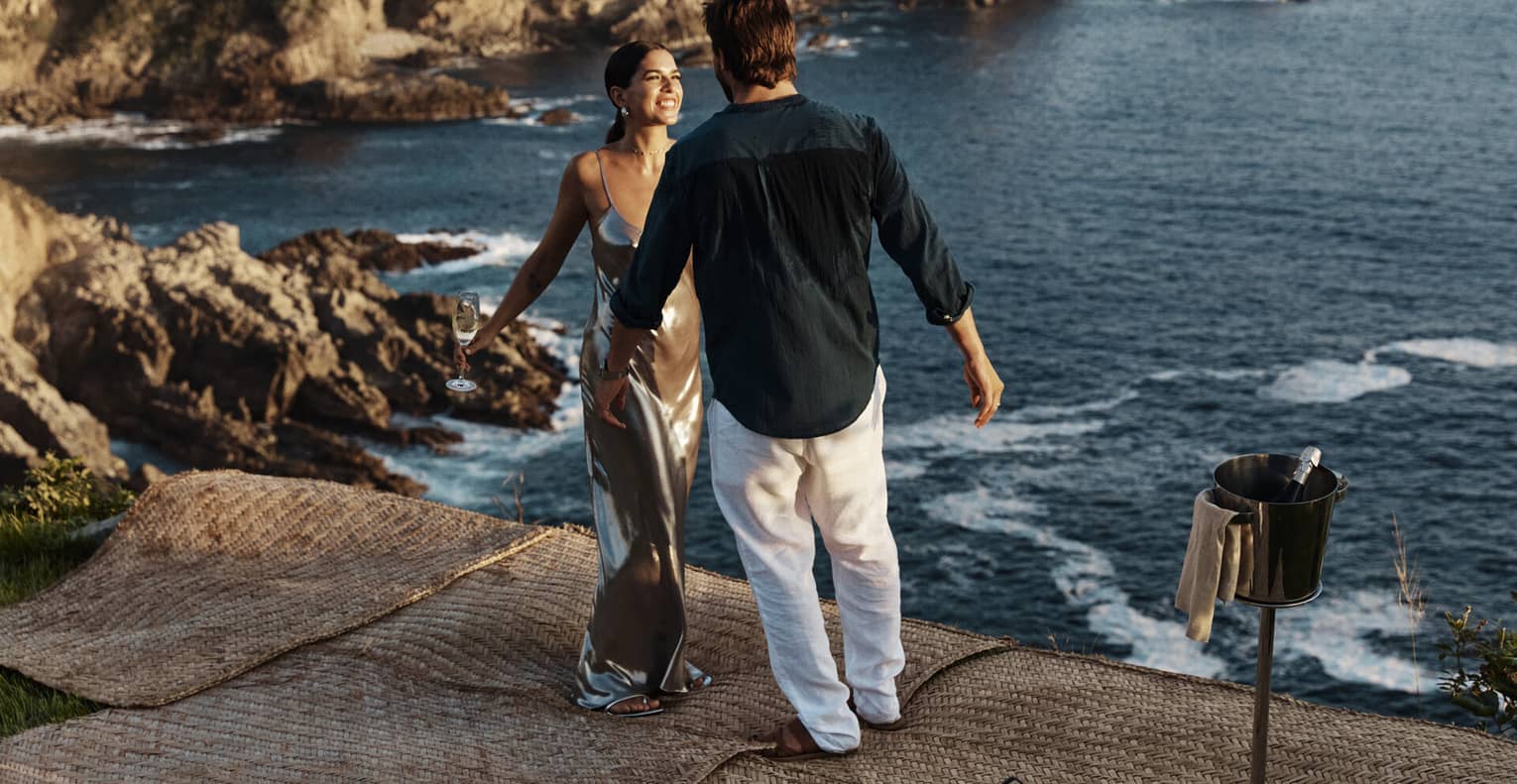 A couple standing near a vast, shimmering ocean against a backdrop of majestic cliffs, embraced by the beauty of nature