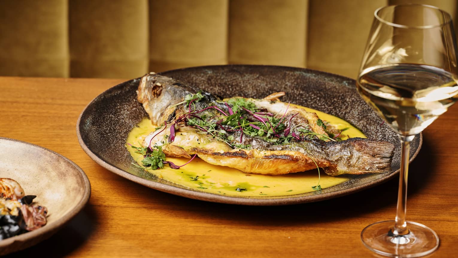 Whole fried Branzino dish and a glass of white wine on a wooden table