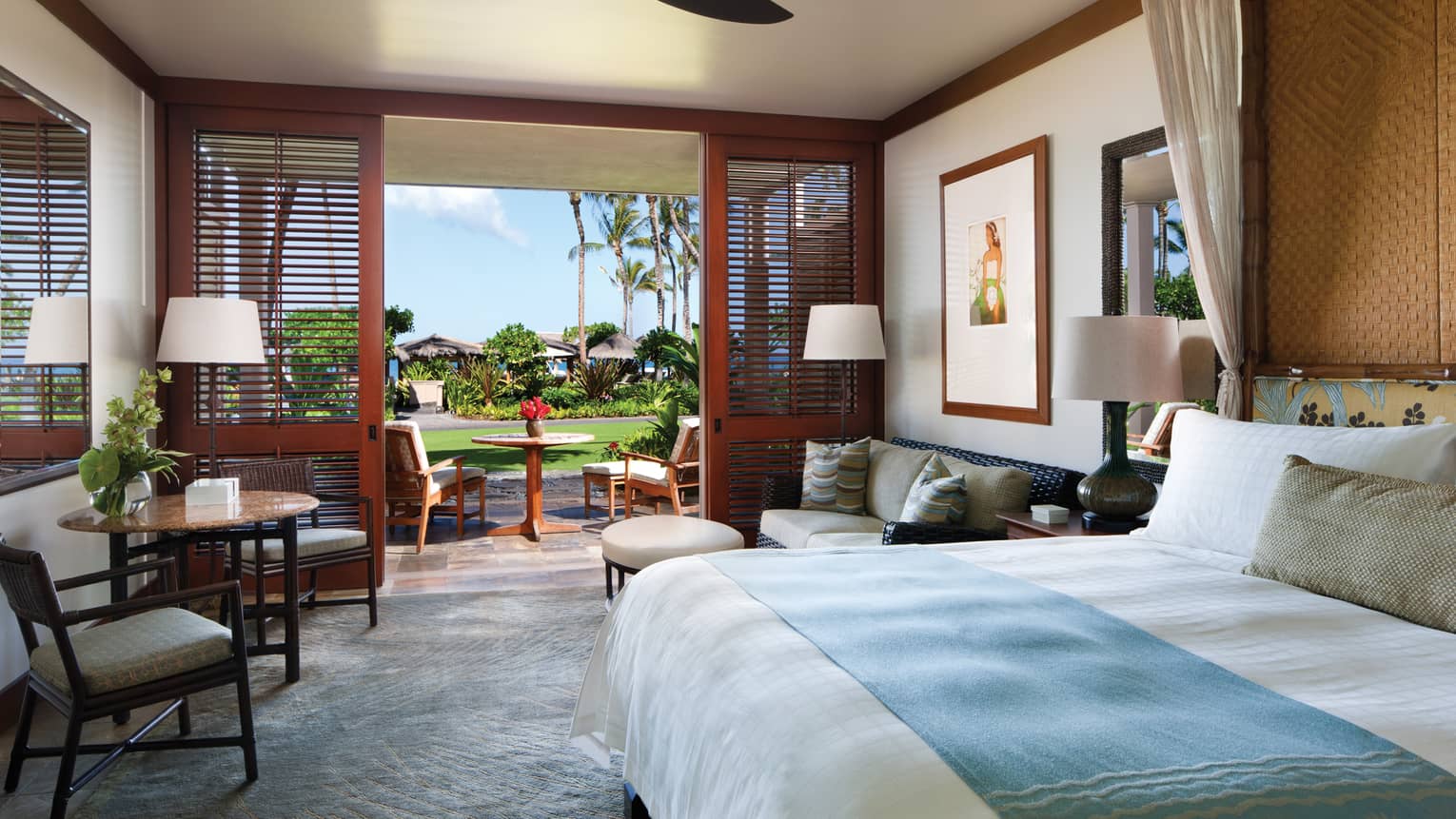 Partial Ocean-View Room bed with blue blanket, loveseat, cafe table by open wall, wood shutters