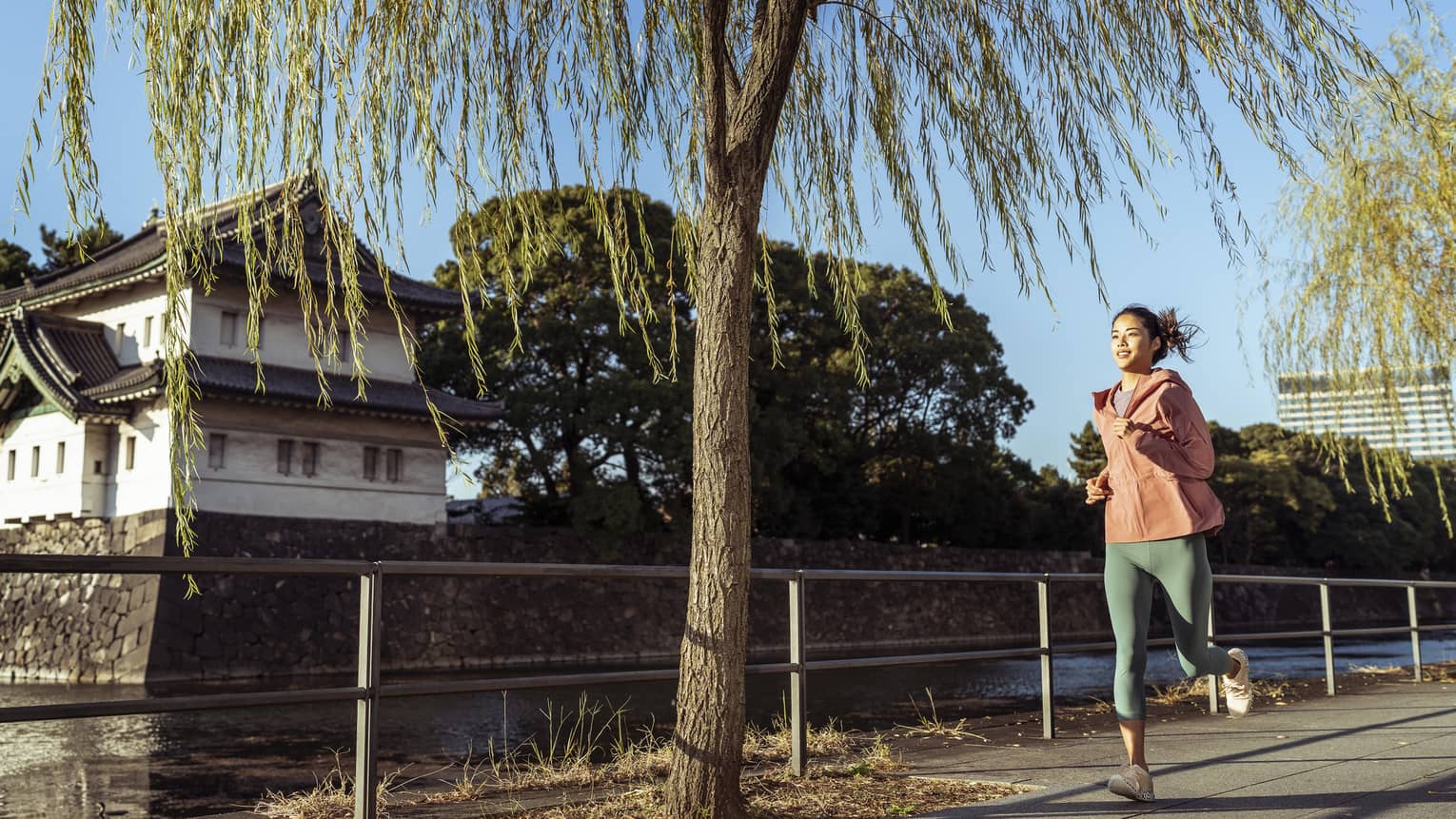 Woman jogs by Japanese temple and moat