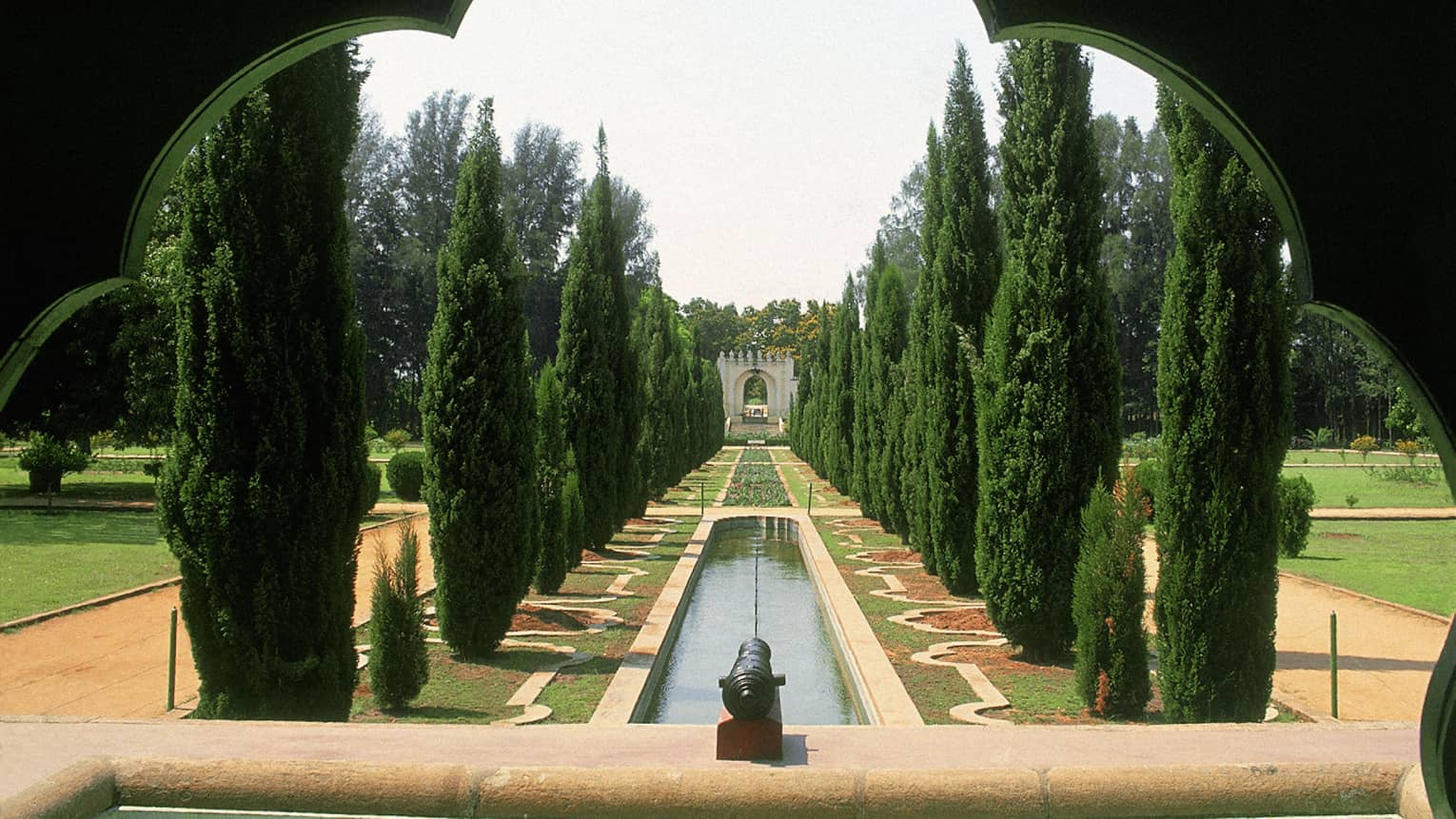 Thin trees line a strip of water and flowers in Tipu Sultan's Gardens