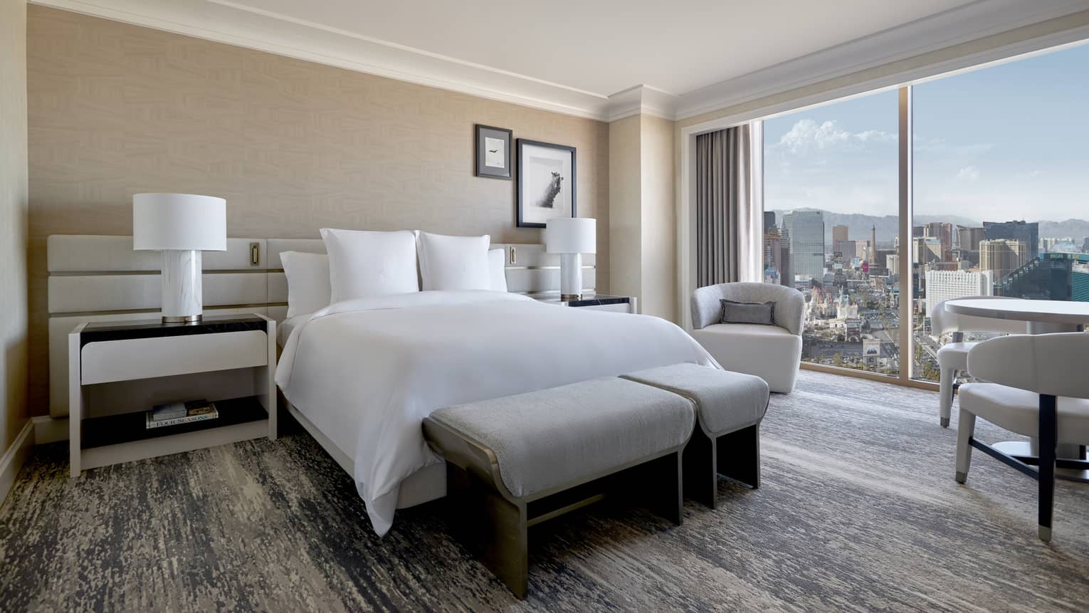 A guestroom with bed, large window, two side tables, chairs and table.