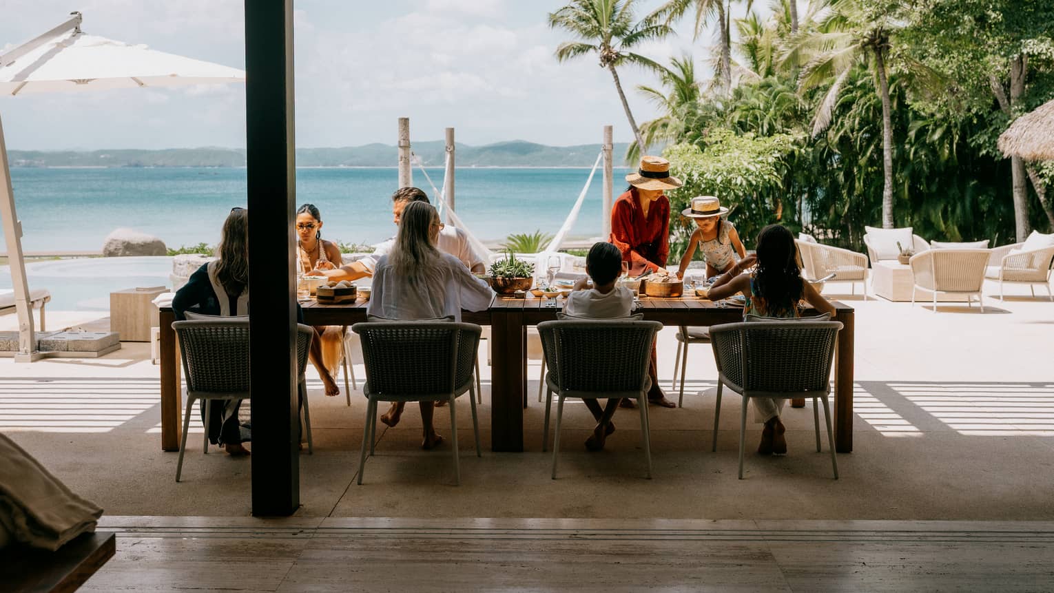 A group of people enjoy a meal in an outdoor dining setting looking out over the beach and ocean.
