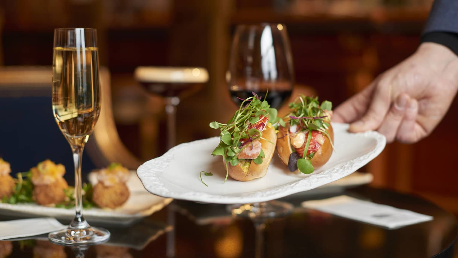 Two lobster rolls on a white plate being set on a dining table