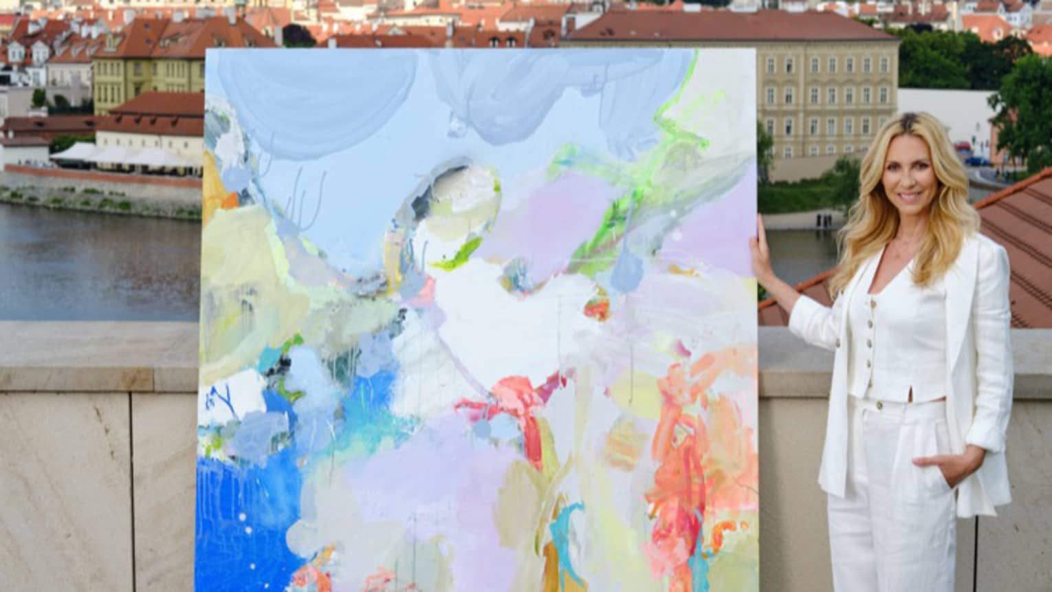 A person standing next to a large abstract painting on a terrace with a view of Prague Castle and the city skyline in the background.
