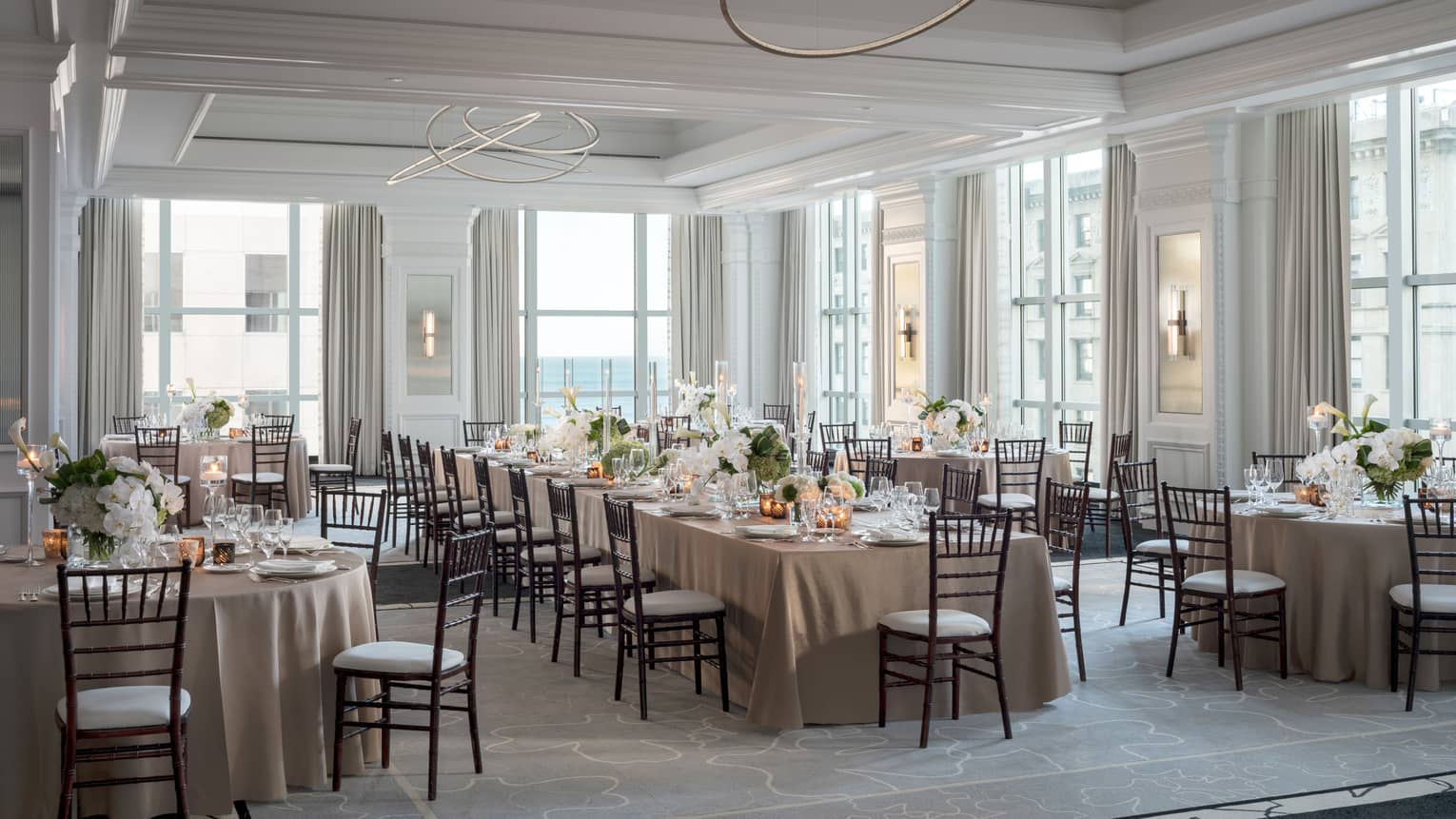 Ballroom with high ceilings and large windows, one long table surrounded by round tables