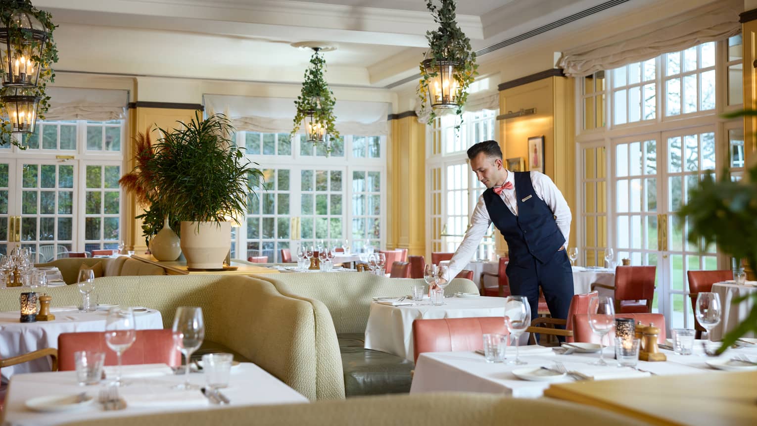 Server sets wine glass on table in elegant, bright restaurant dining room