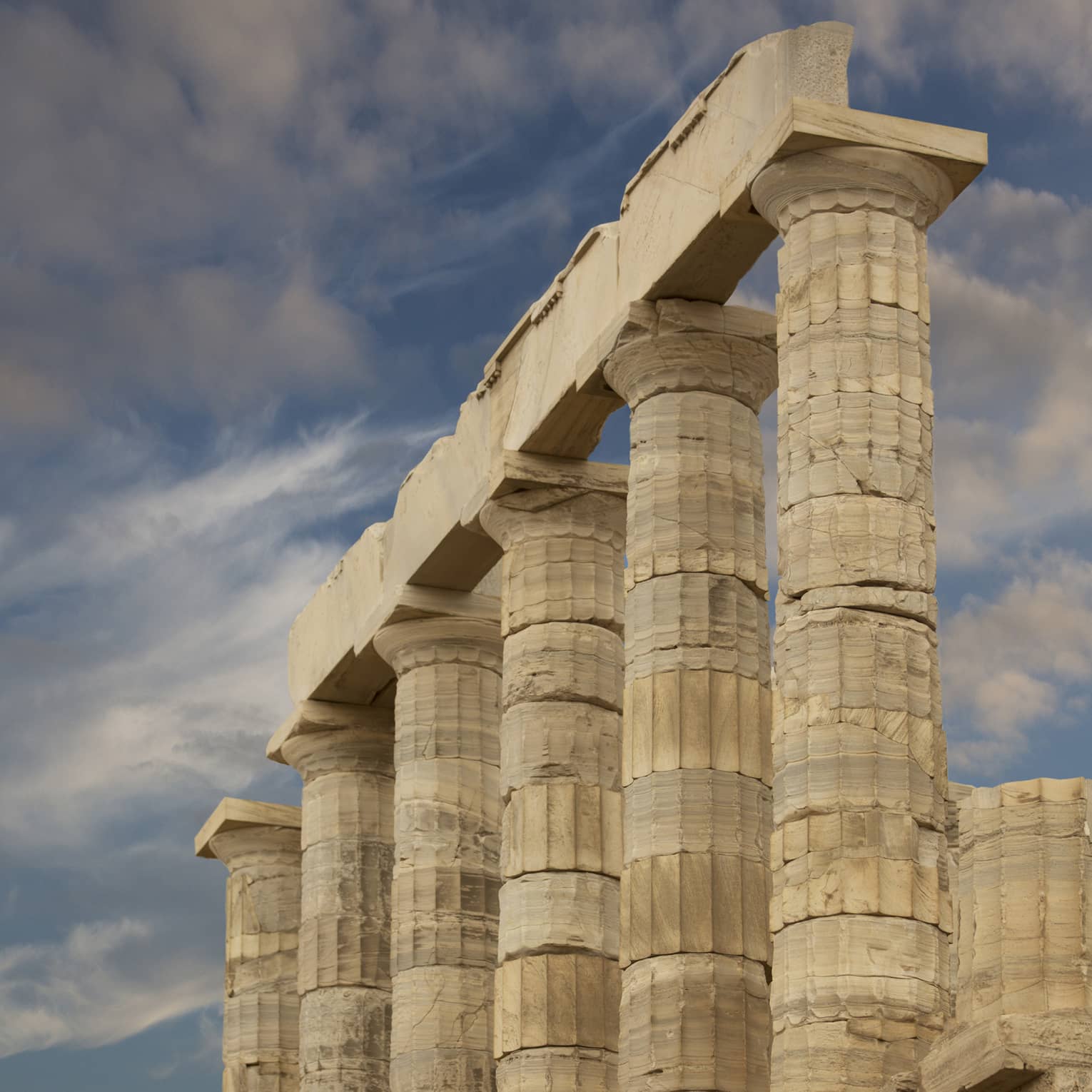 From the bottom of stairs, view of ancient towering Doric columns with vertical grooves atop a jagged brick foundation.