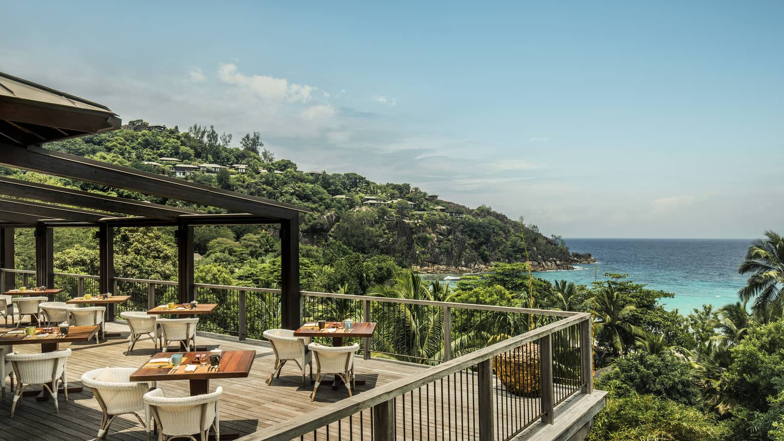 ZEZ outdoor dining room on wood deck overlooking palm trees, blue sky