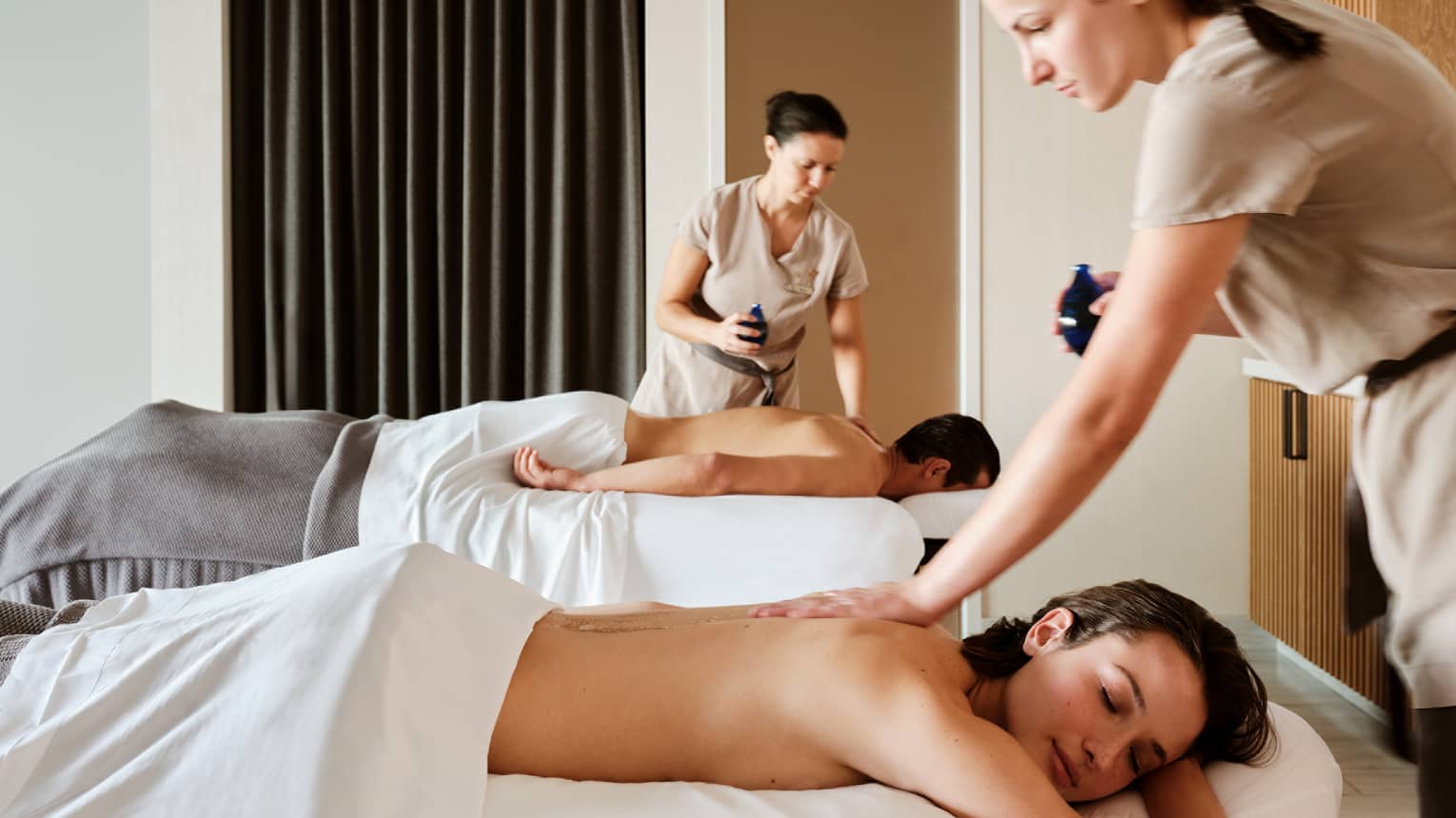Couple lying prone on spa tables while being massage by spa therapists