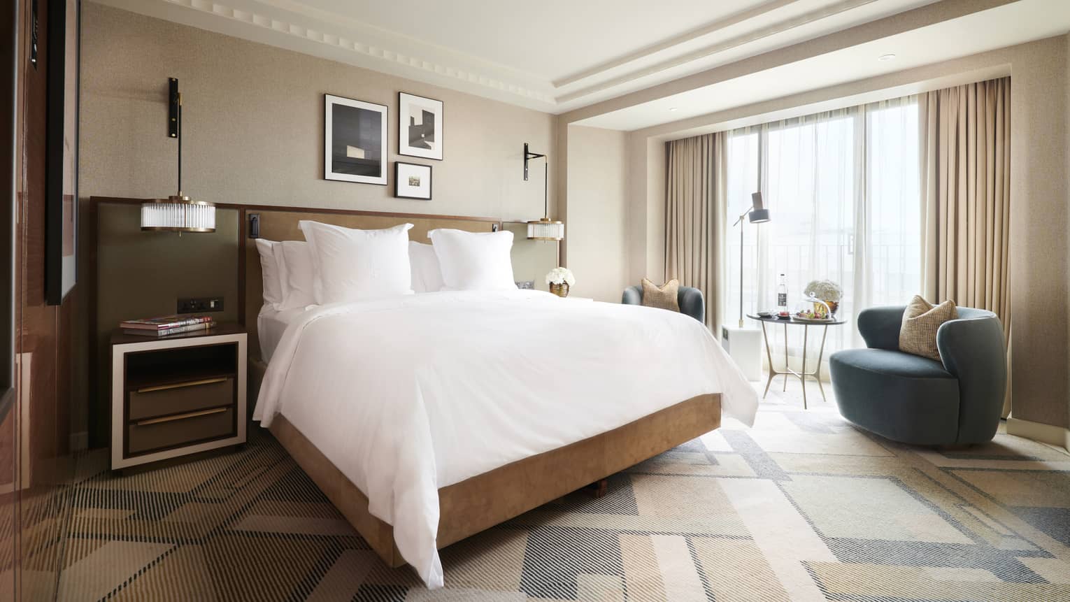 Deluxe room at the Four Seasons London Park Lane in Mayfair, featuring a spacious and well-appointed interior. The room includes a large king-sized bed with white linens and plush pillows, flanked by bedside tables and elegant wall-mounted lamps. A cozy seating area near the window includes a stylish blue armchair and a small circular table with chairs, ideal for relaxing or enjoying the view. The room's decor is enhanced by soft, neutral curtains, tasteful artwork on the walls, and a sophisticated, modern design.,Deluxe Room at Four Seasons London Park Lane in Mayfair, featuring a spacious and well-appointed interior. The room includes a large king-sized bed with white linens and plush pillows, flanked by bedside tables and elegant wall-mounted lamps. A cosy seating area near the window includes a stylish blue armchair and a small circular table with chairs, ideal for relaxing or enjoying the view. The room's decor is enhanced by soft, neutral curtains, tasteful artwork on the walls and a sophisticated, modern design.