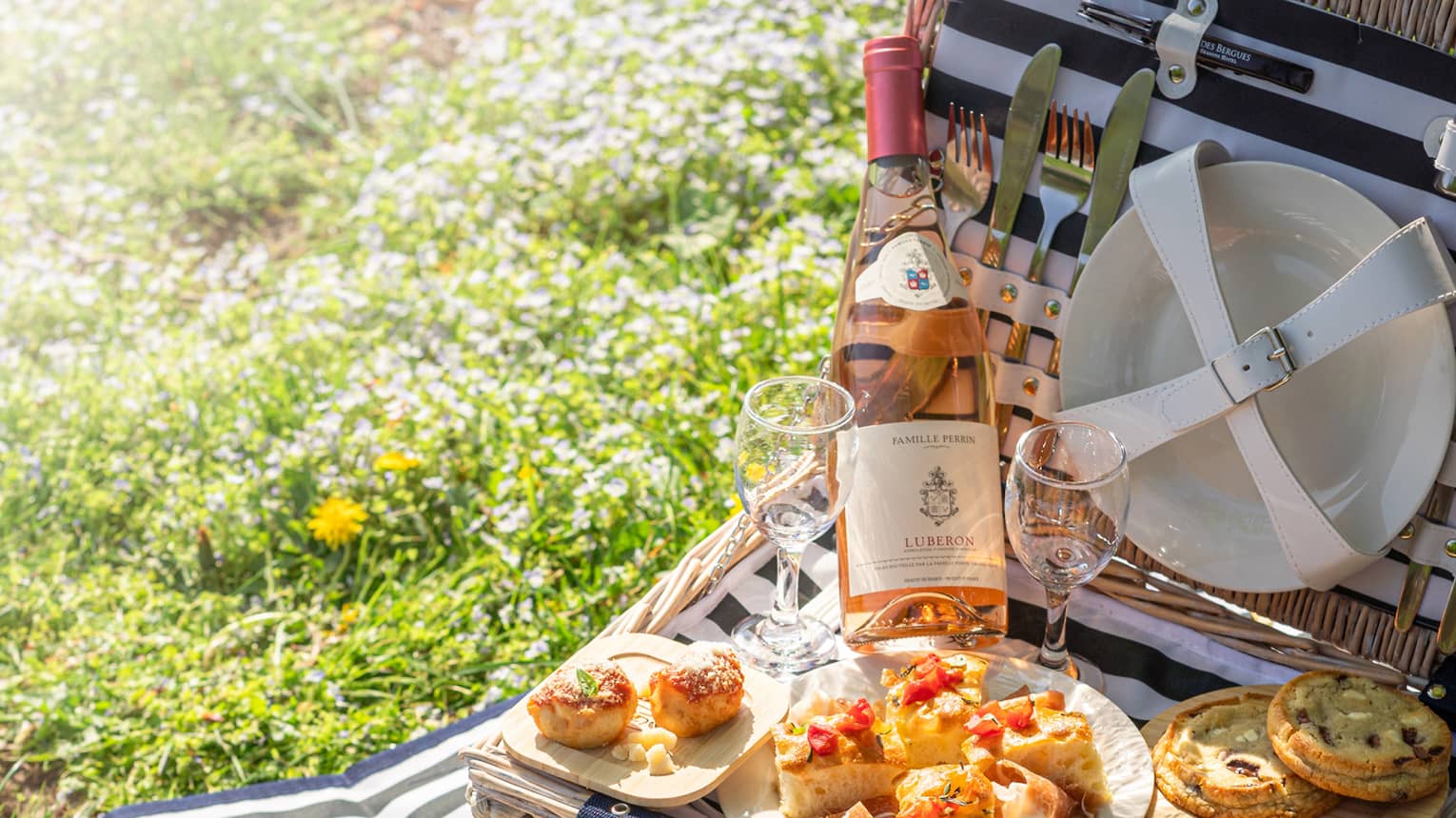Open picnic basket with wine and plates of shrimp, bread and fruit.