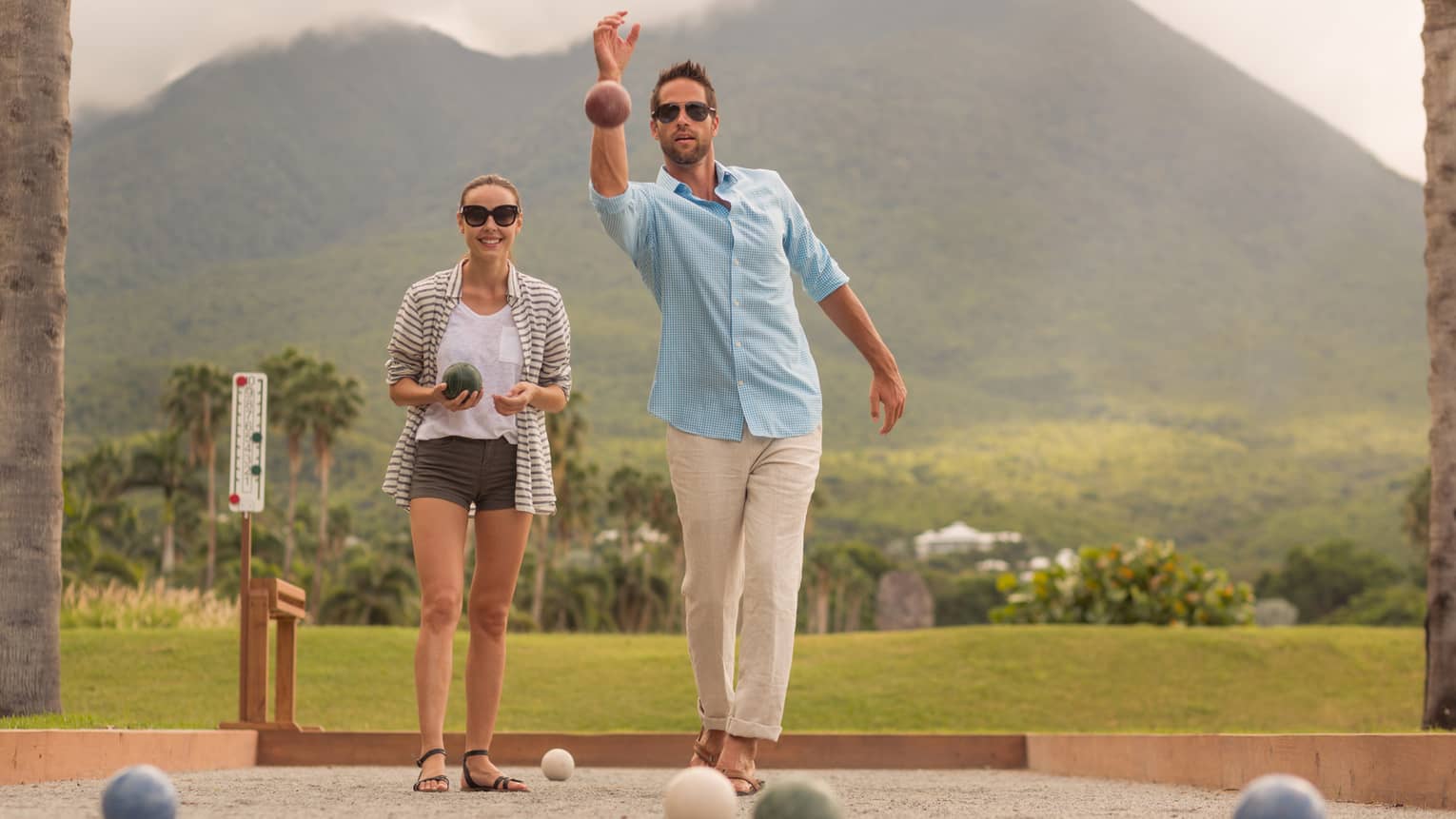 Man and woman lawn bowling, tropical mountain in background