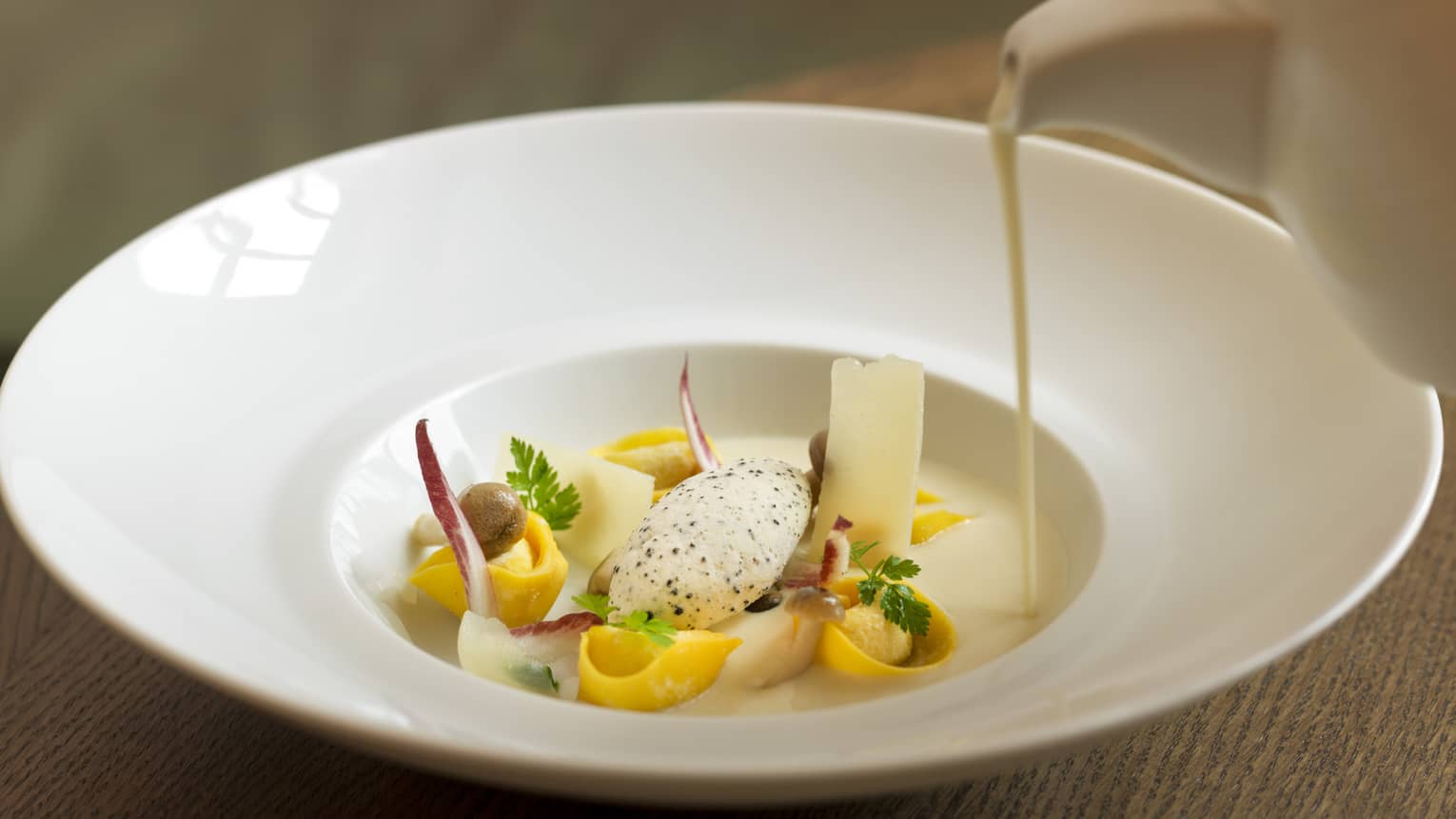 Cream soup being poured into white dish with gourmet ingredients