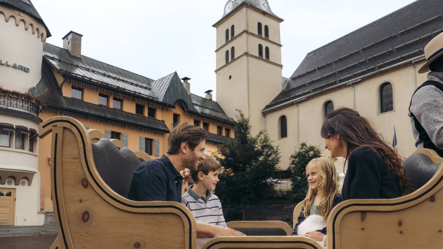 Family of four sitting in a horse-drawn carriage with historic building in background