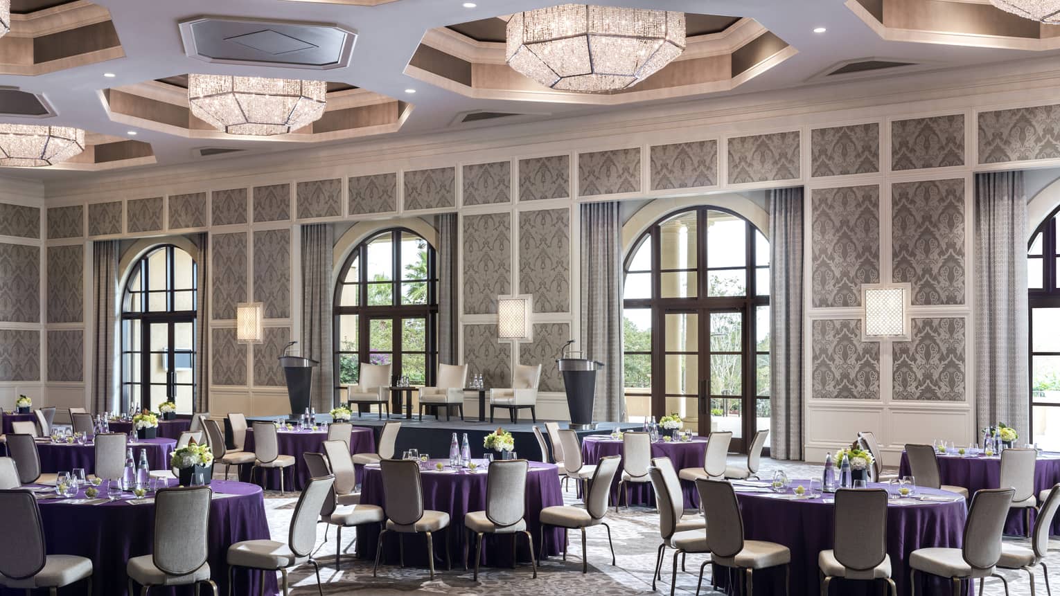 Grand Ballroom with round banquet tables under geometric chandeliers, sunny arched windows 