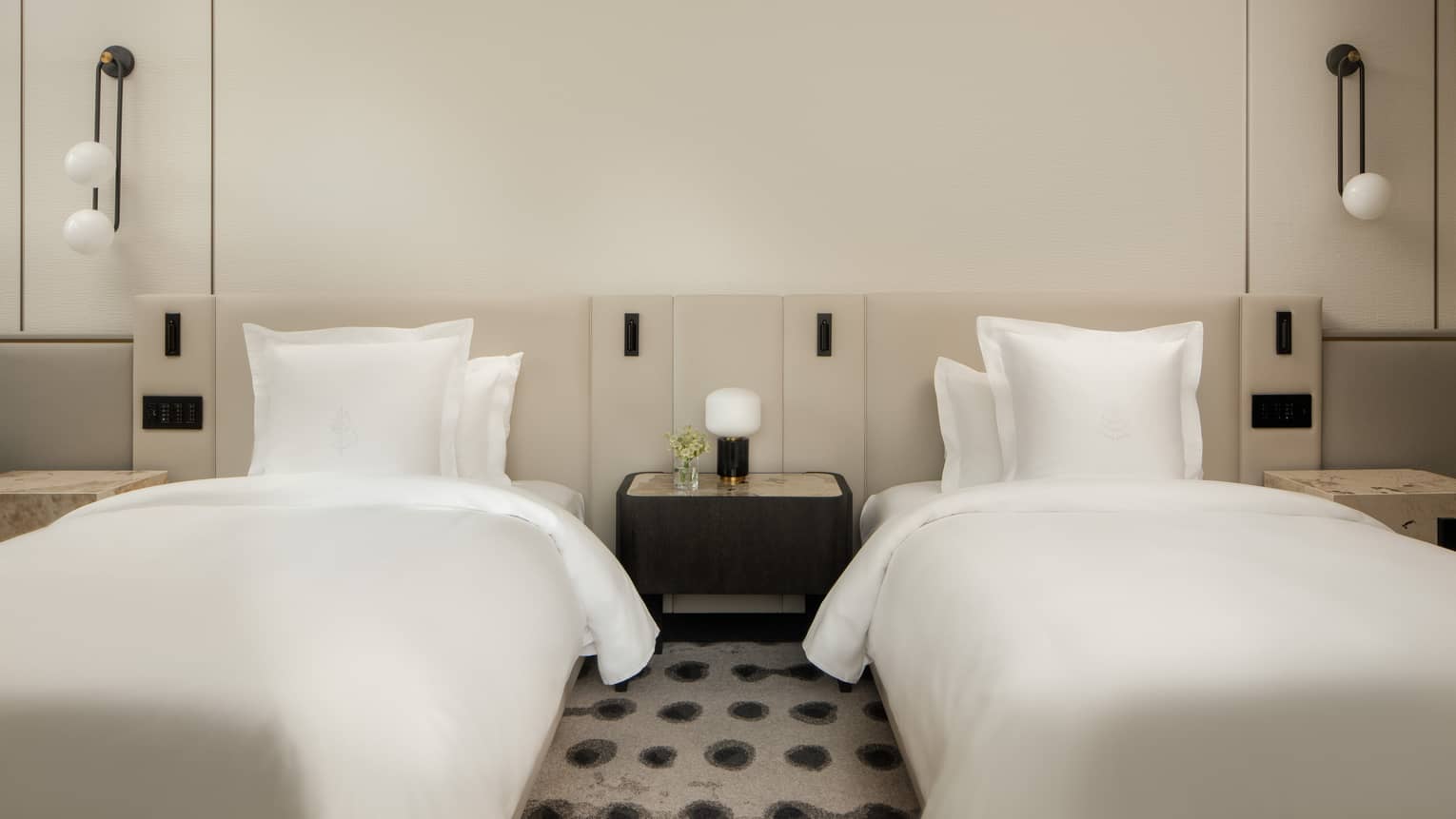 Luxury hotel room with two double beds, white linens, a shared nightstand, wall-mounted lights, featuring minimalist décor 