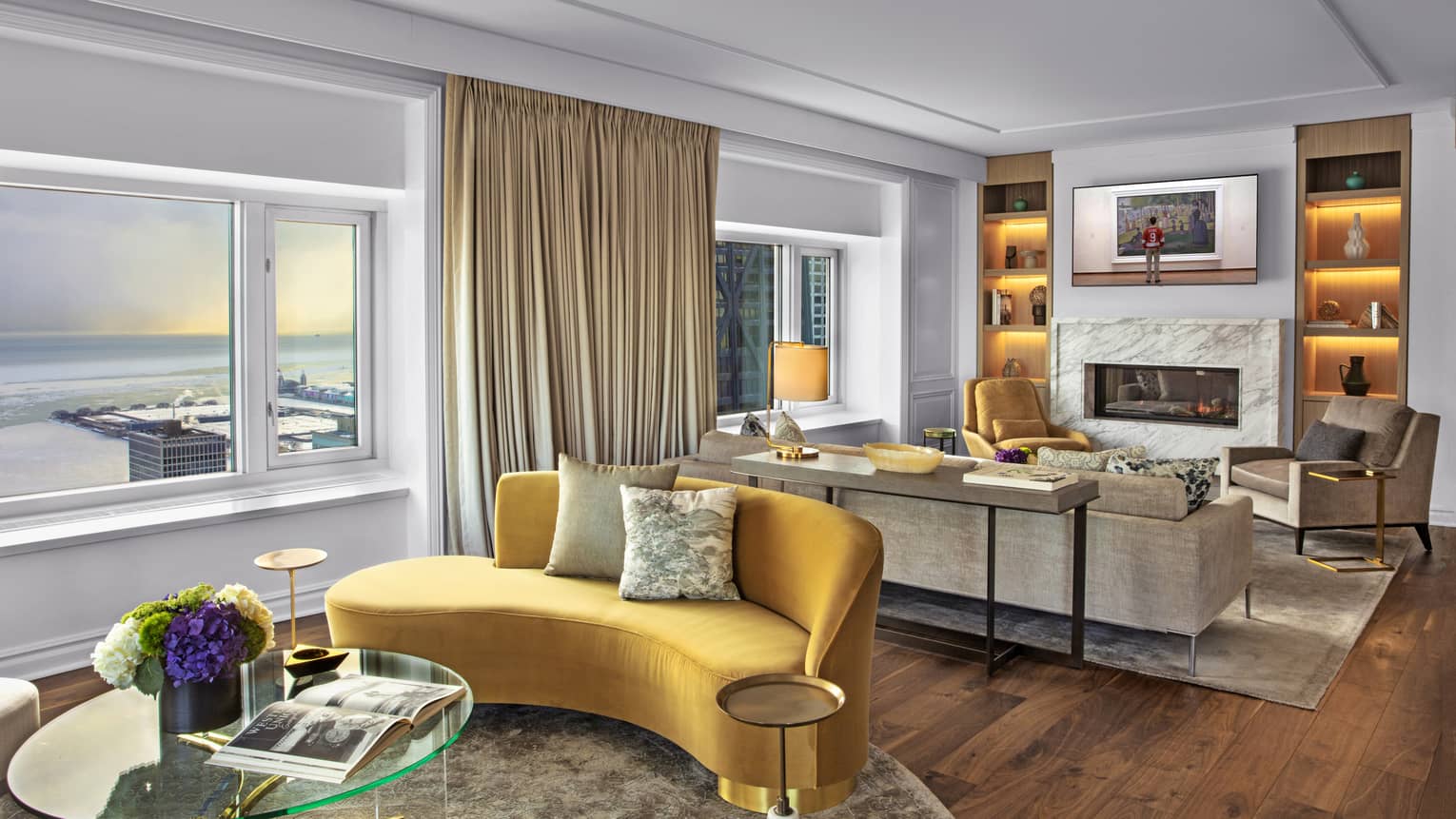Suite with a yellow couch and glass table, as well as a television and fireplace.
