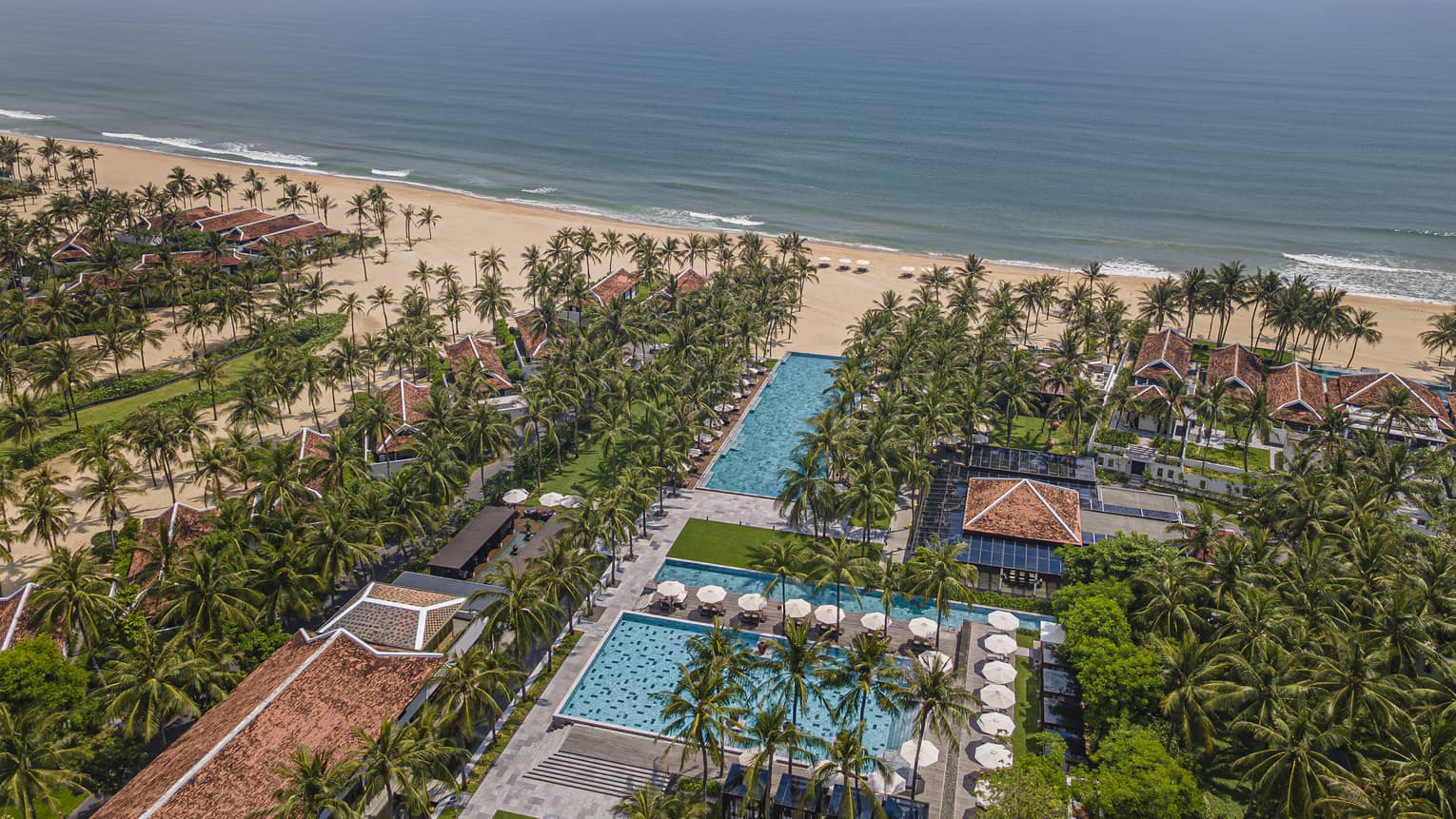 Aerial view of beachside property with pools, palm trees and ocean views