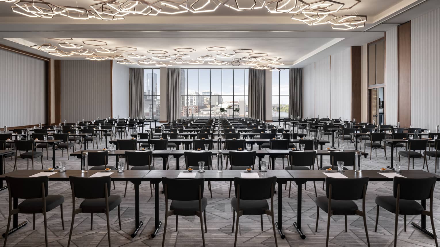 A large meeting room with many tables and chairs, geometric lights and large windows.