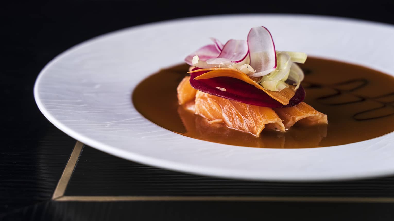 Salmon Tataki garnished with a beetroot slice, shaved carrot ribbon, and ginger and radish slices