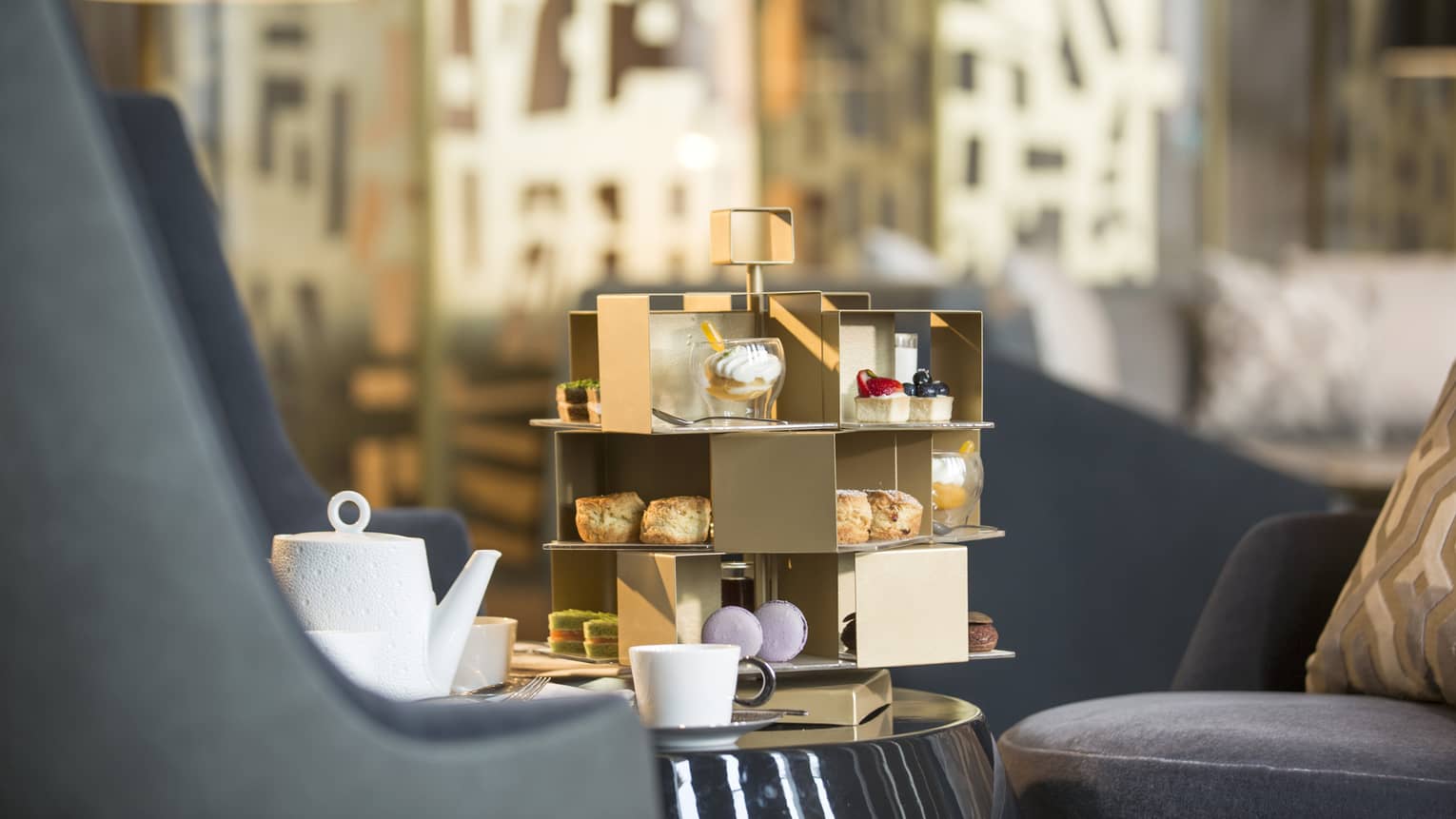 Afternoon Tea gourmet desserts on gold stand, white teapot and cup on lounge table
