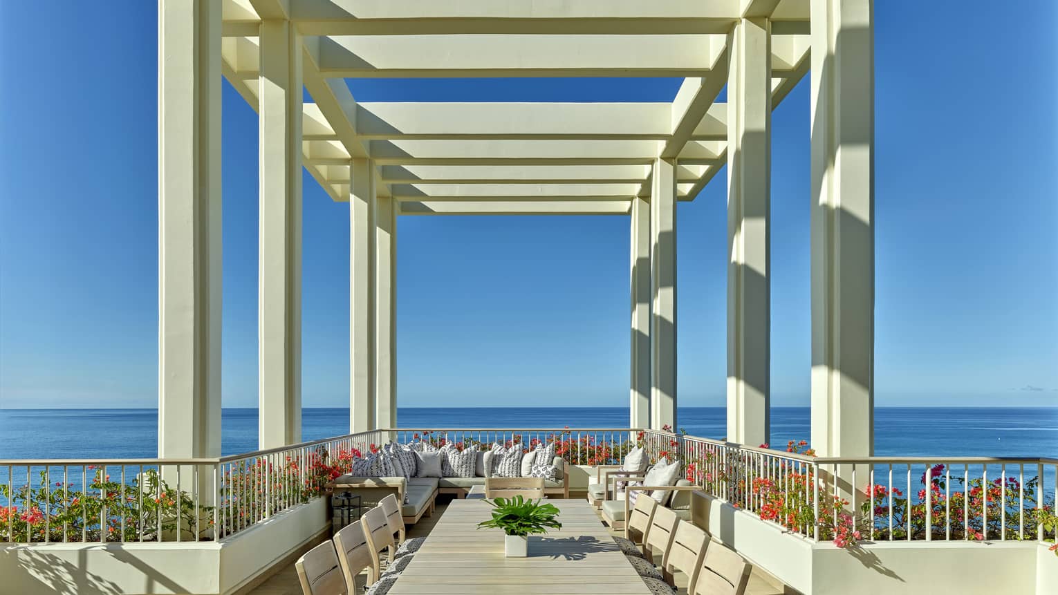 Ocean-view terrace with long dining table under pergola