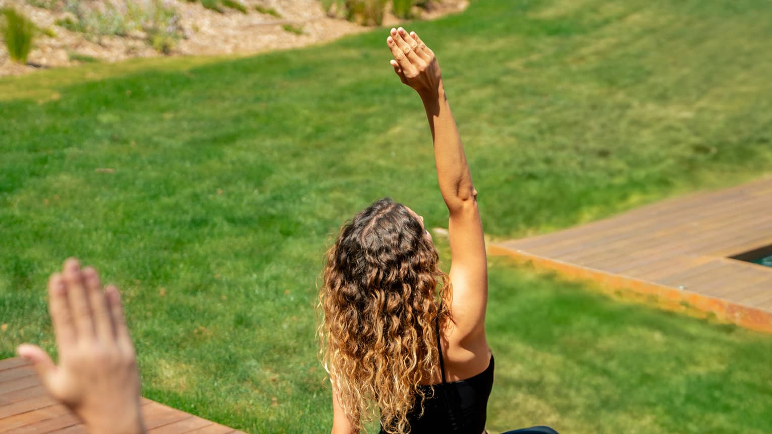 Two people in yoga pose practise on outdoor wooden deck overlooking lush green grass