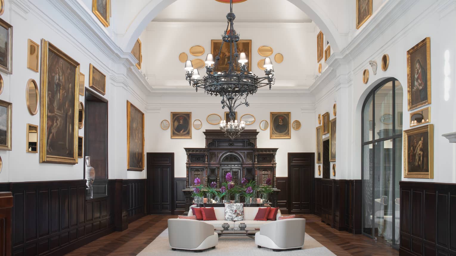 Sala Museo with artwork lining both walls, white leather furniture, high ceilings, wrought iron chandelier, fireplace