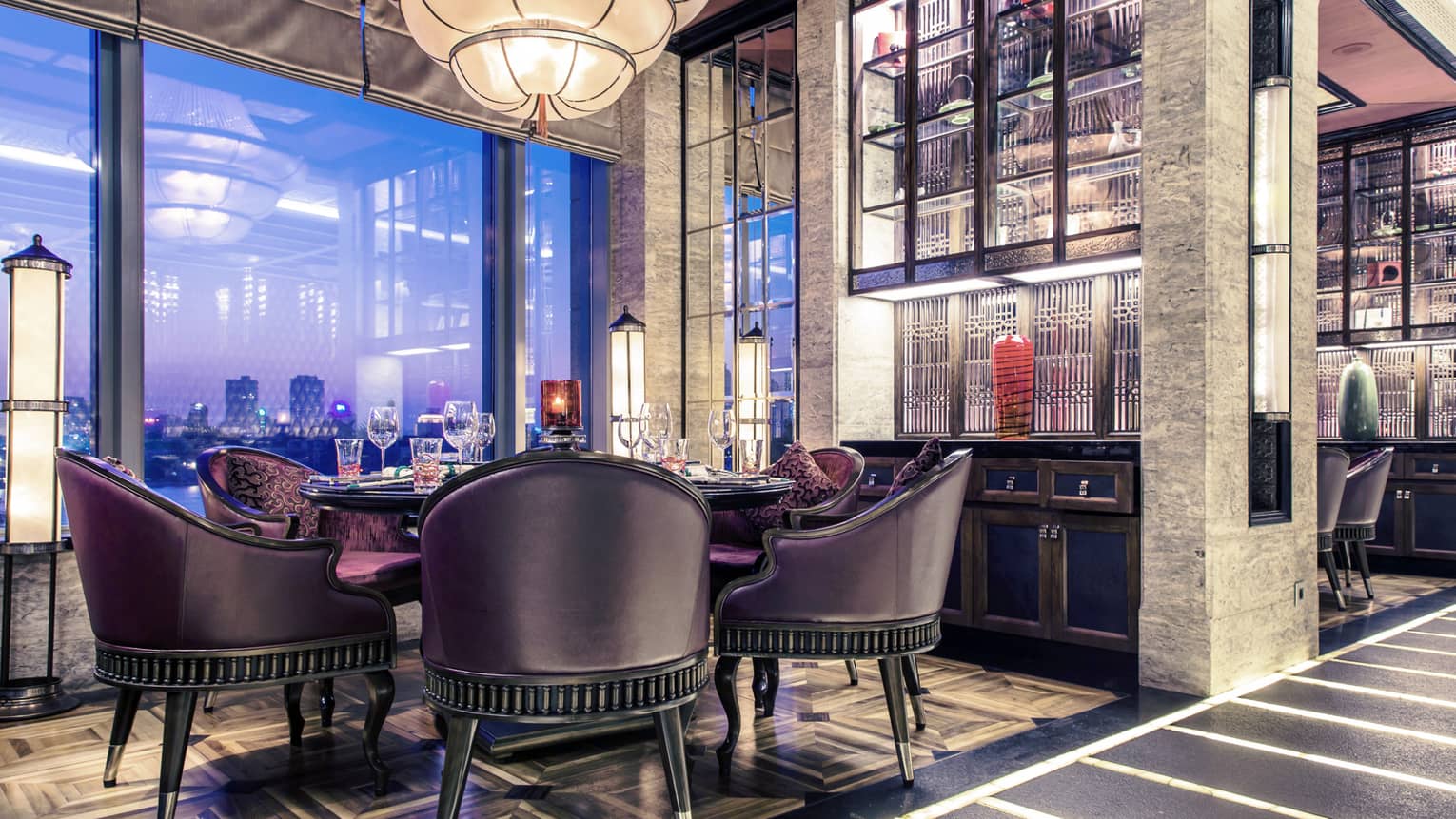 Dining table with black leather and purple velvet bucket-style chairs under tiered, cone-shaped chandelier 