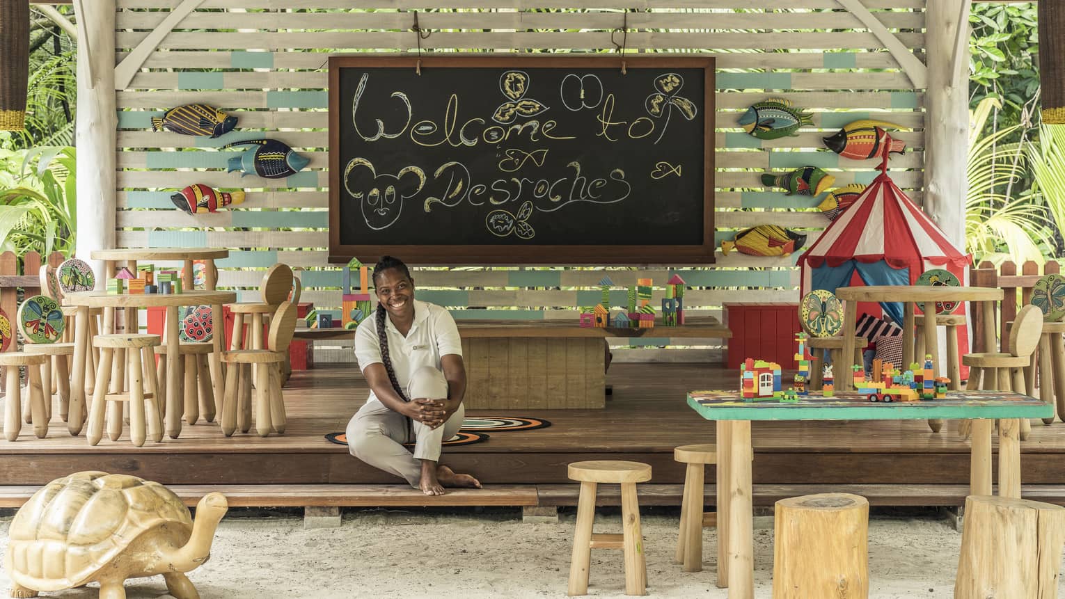Kids Club play area with chalkboard, fish accents and tables, and a smiling staff member seated