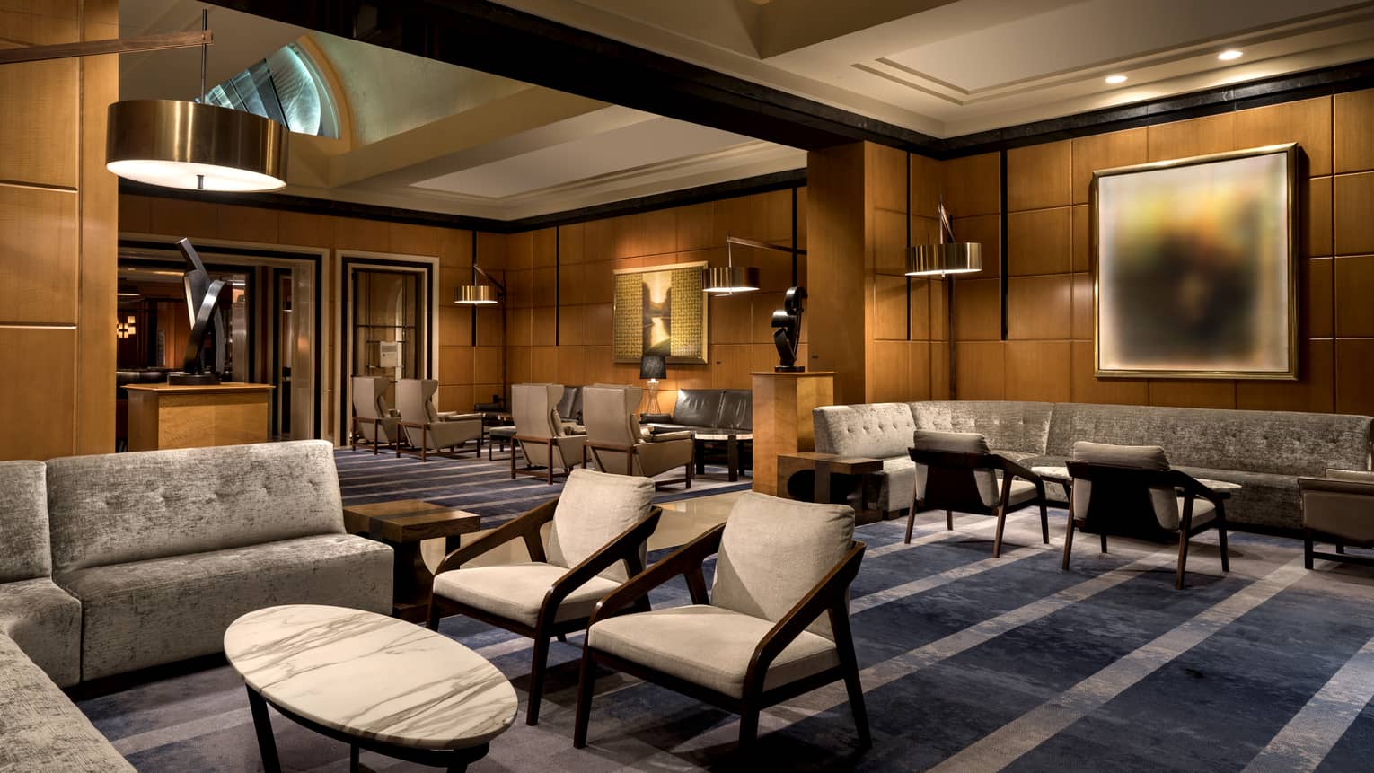 A lounge and lobby area with dark blue carpeting, grey chairs and sofa, and wood walls.