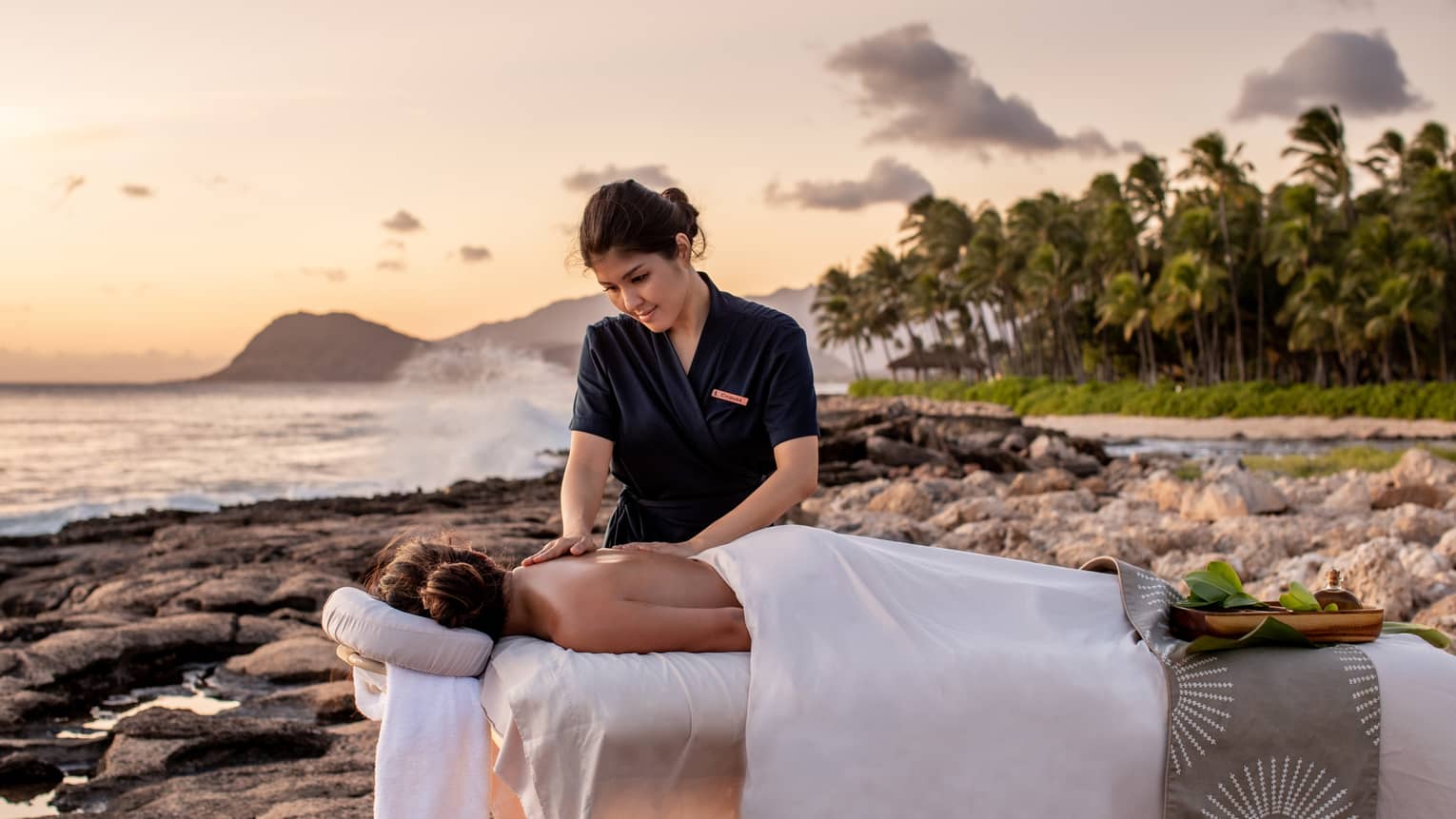 A four seasons guest receives a massage on the beach, as the sun sets in the distance