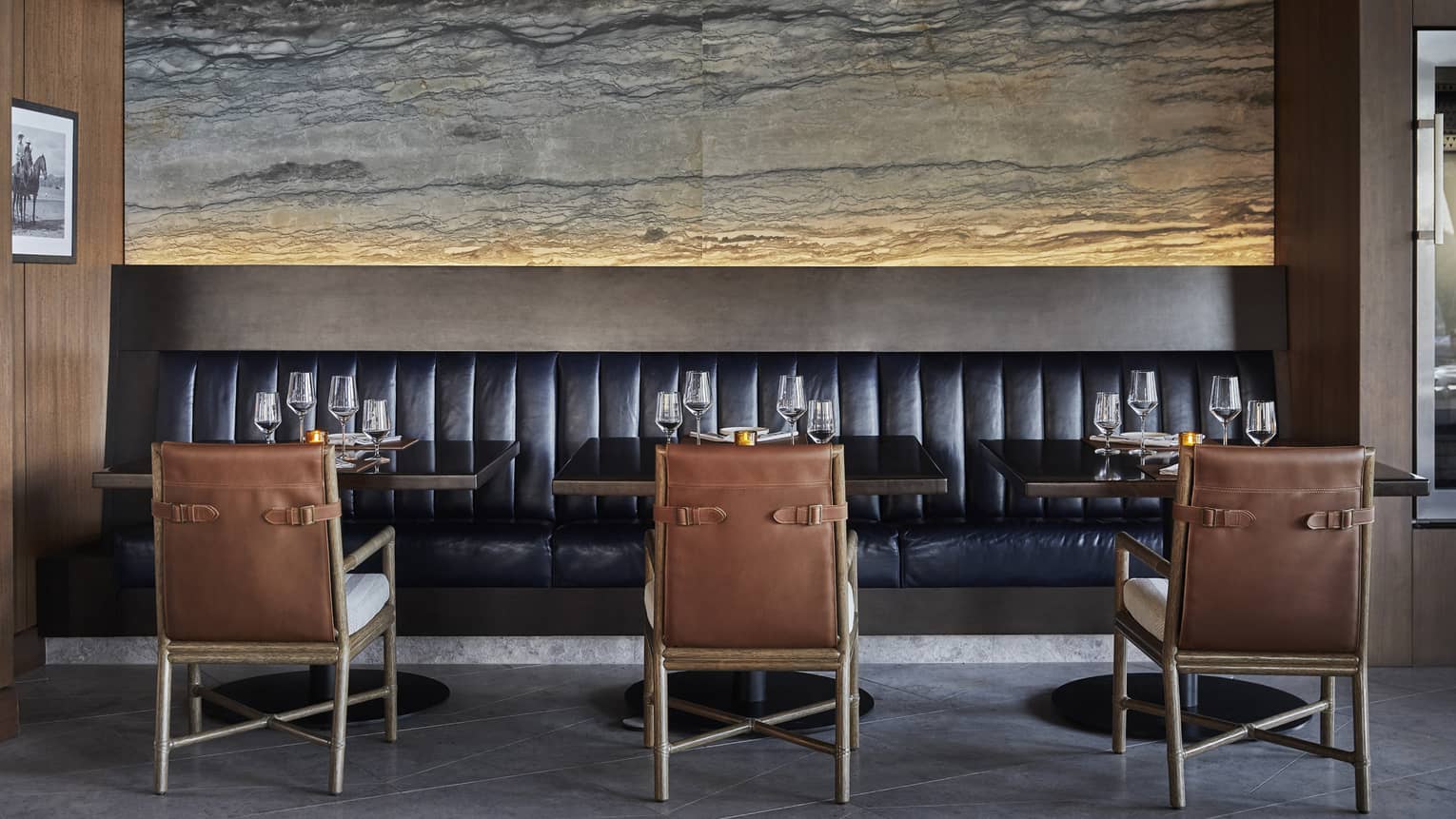 Three brown chairs face a black booth in a dining room.