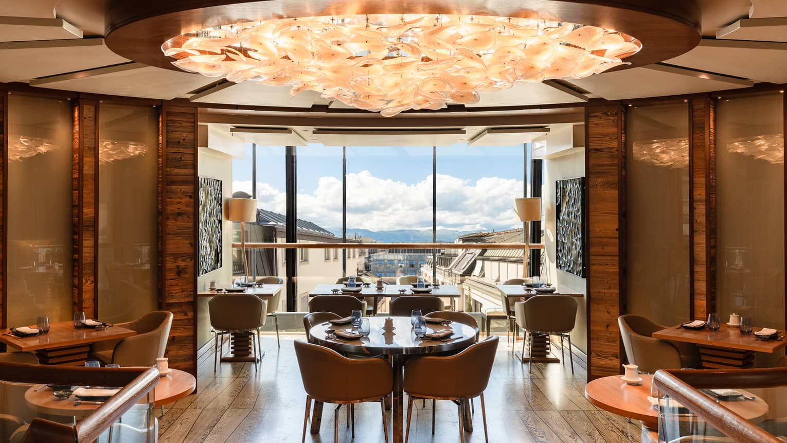 Curved, wood-panelled walls encircle a dining room with a peach-coloured chandelier and windows showing distant mountains.