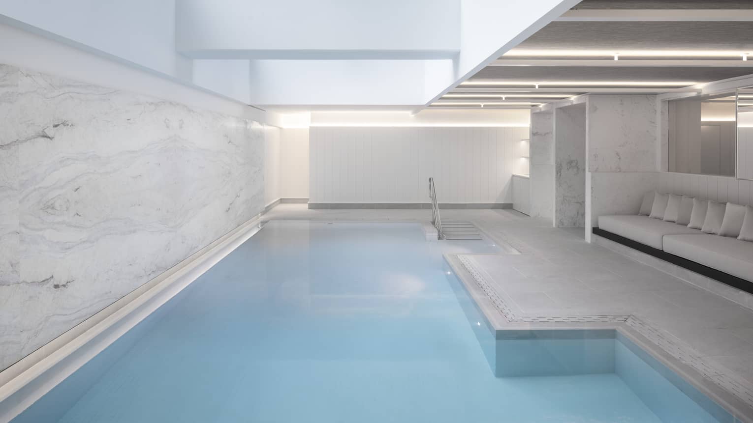 Indoor pool at spa, banquet of seating on one side, marbled wall on other 