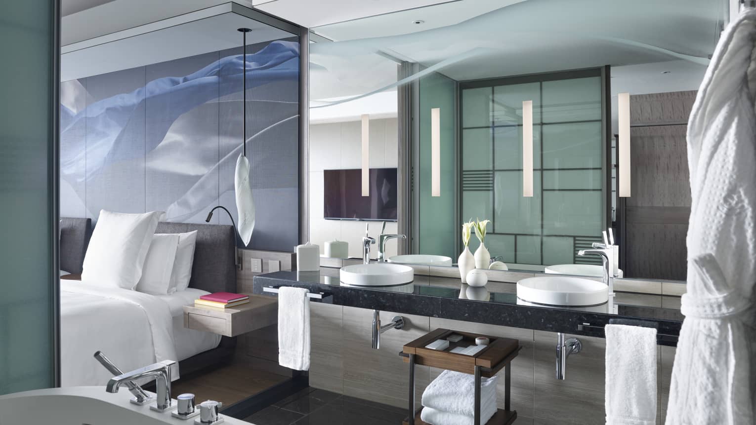 Modern bathroom with a double-sink vanity, large mirror and a partial view into the bedroom area, featuring sleek glass partition