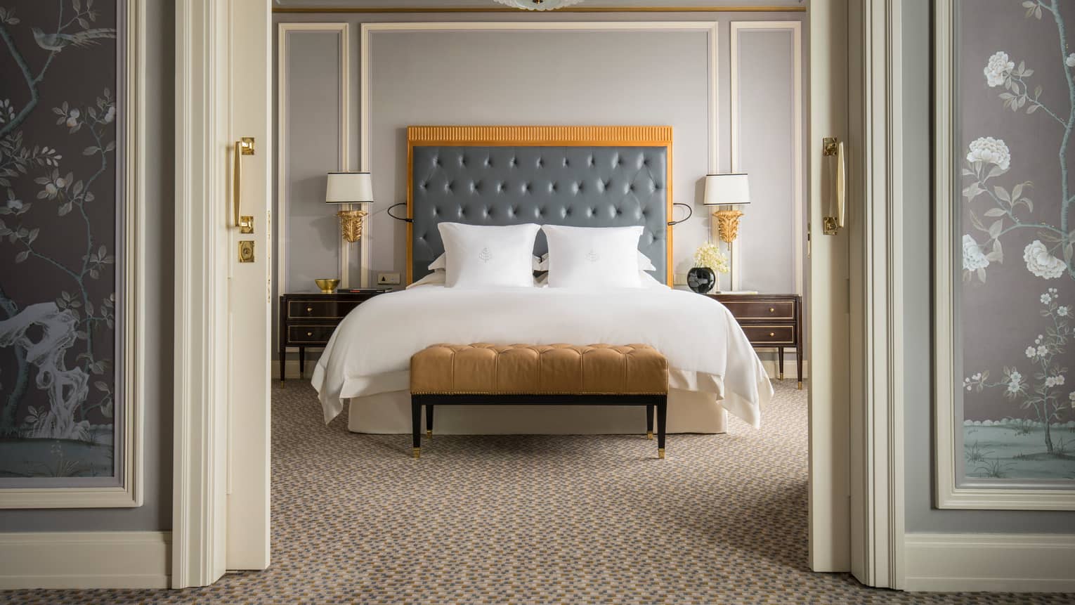 Executive Deluxe Suite front view of king-size bed with tall padded blue headboard, gold velvet bench at foot