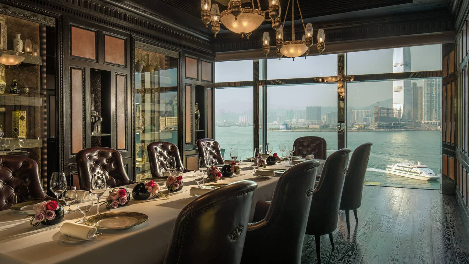 Long private dining table with roses under antique lamps by window overlooking harbour