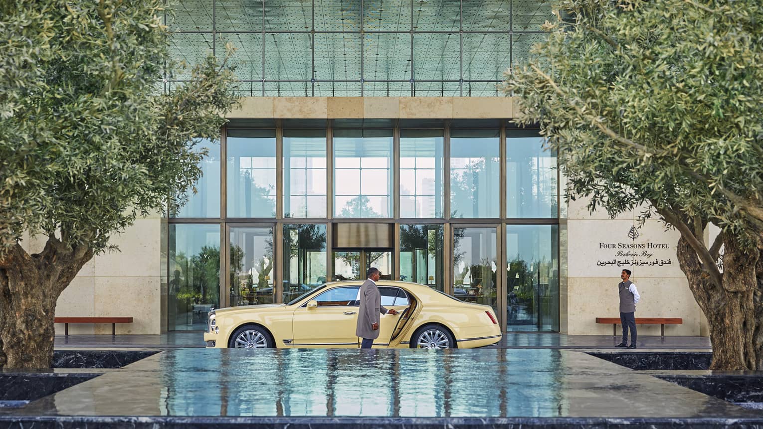 Man opens luxury car door at hotel front entrance by fountain, trees