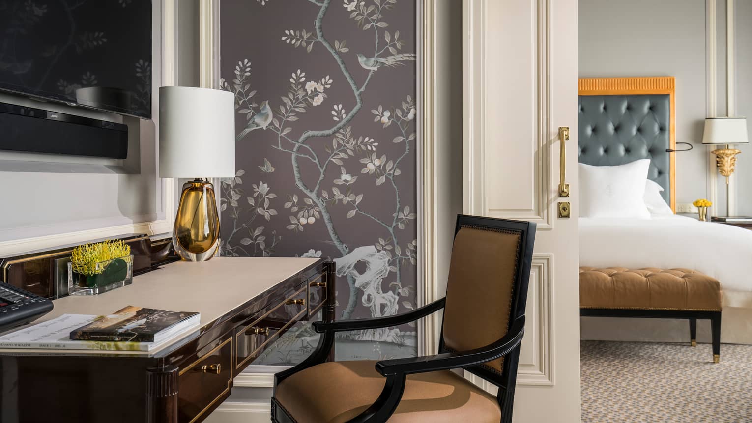 Black desk with orange glass lamp with white shade, wall panel with lilac tone images of trees, birds