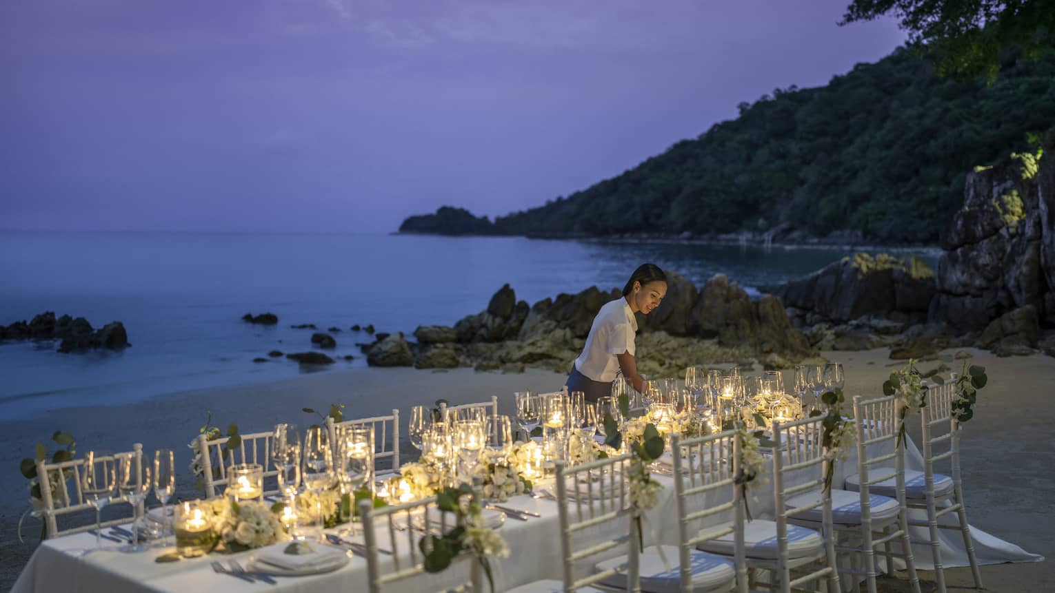 Team member sets up reception table on the beach at dusk