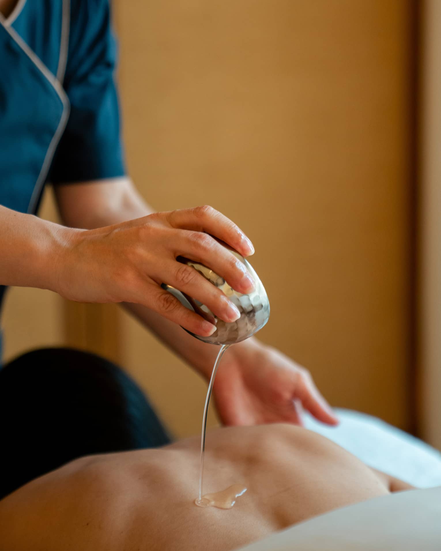 Spa therapist hand pouring oil on person's back