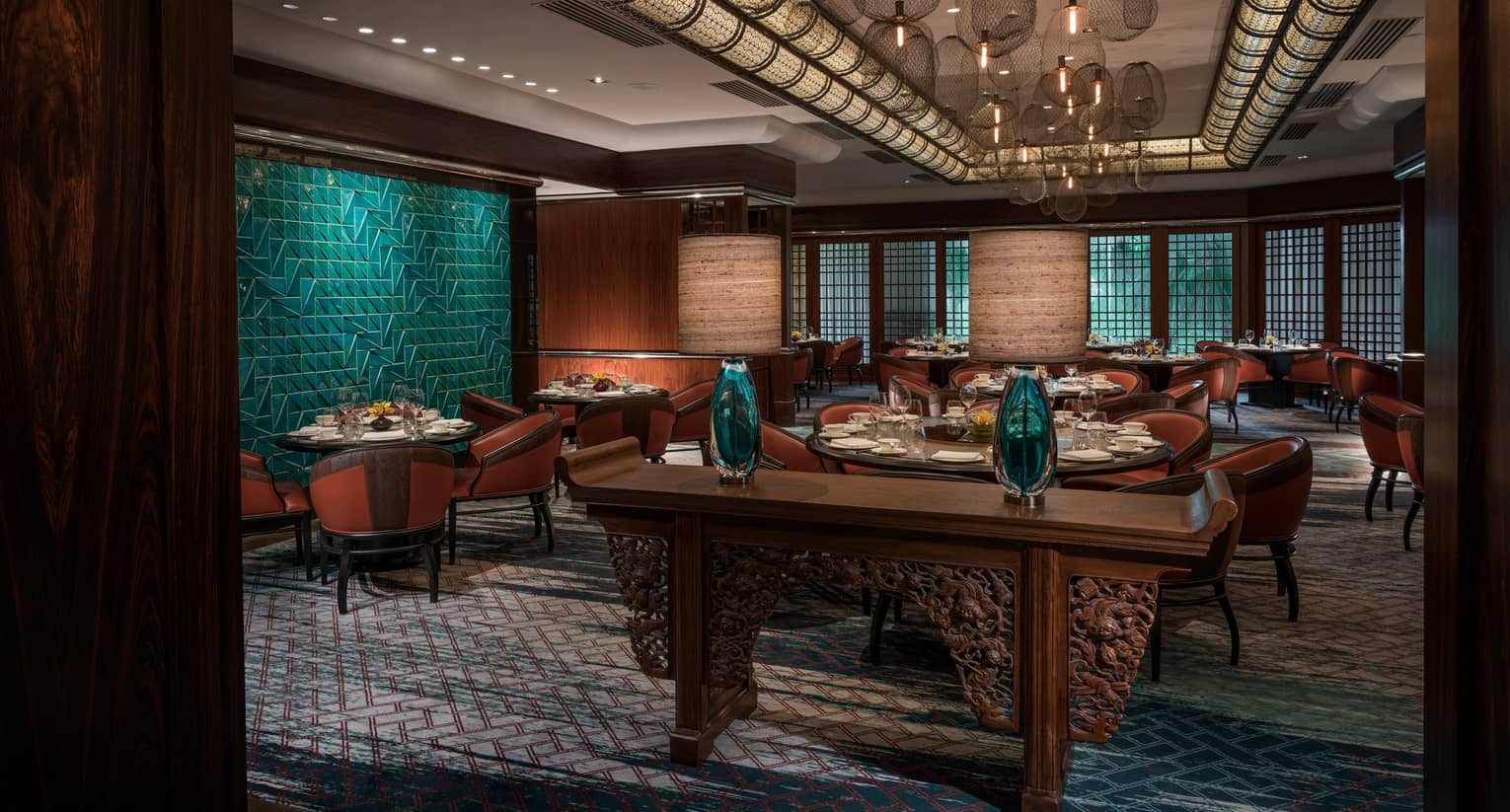 Carved wood console with glass vases in front of dining room, green tile wall