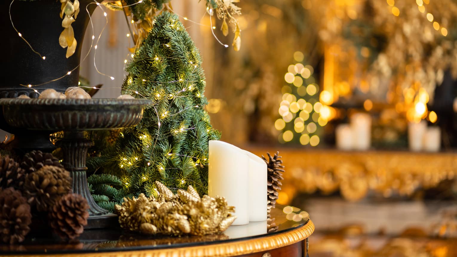 Arrangement of gold-lit mini Christmas trees, white candles and pinecones