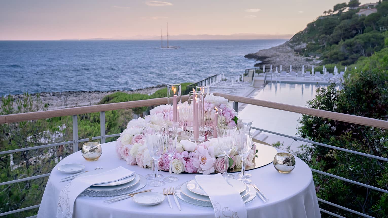 Balcony with round set table, pink floral arrangement, water views at sunset