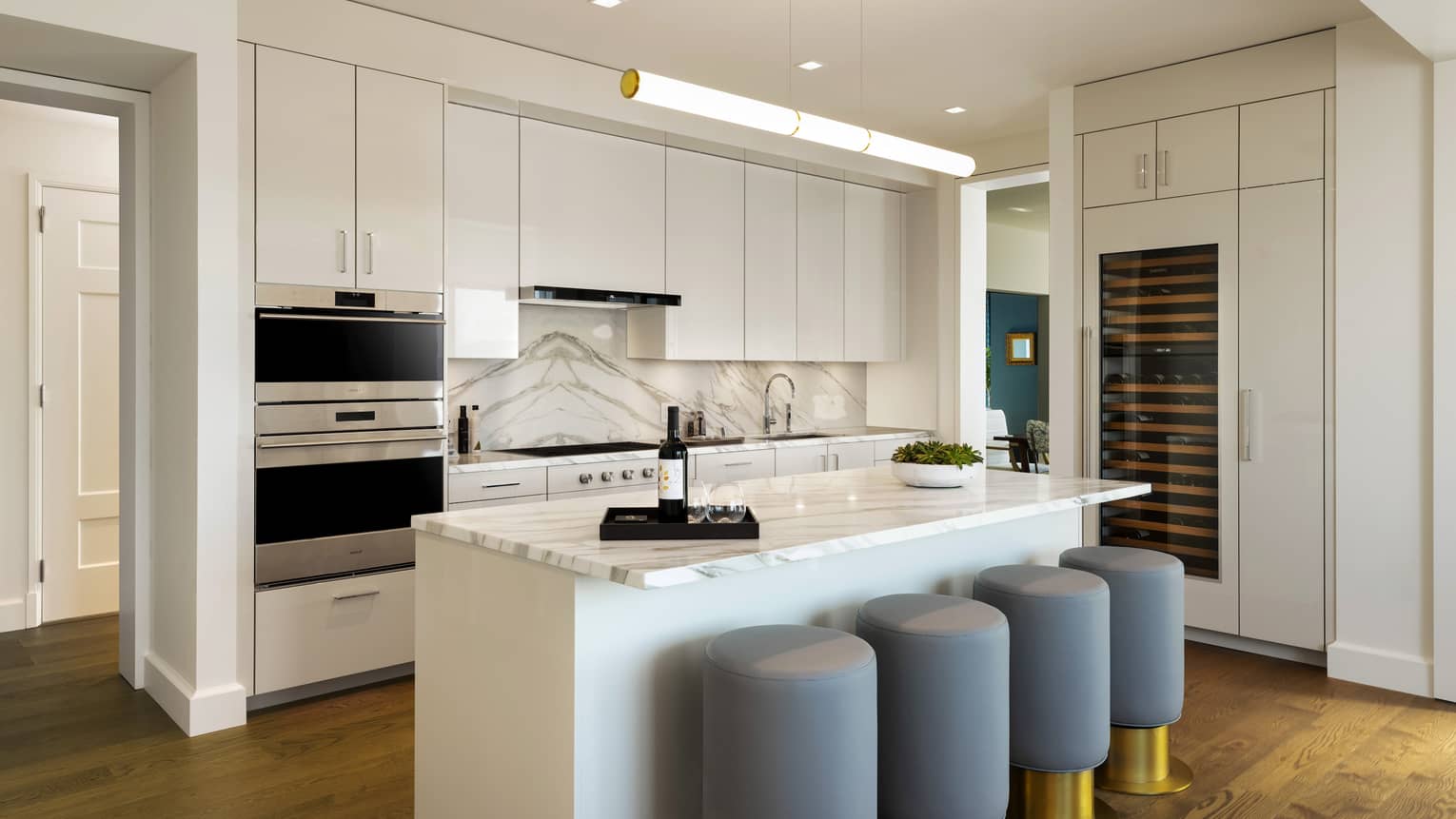 White kitchen with marble countertops, bar stools and glass of wine.